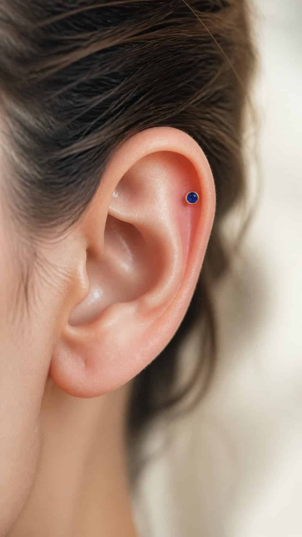 Close-up of an upper ear featuring a small blue birthstone helix stud.