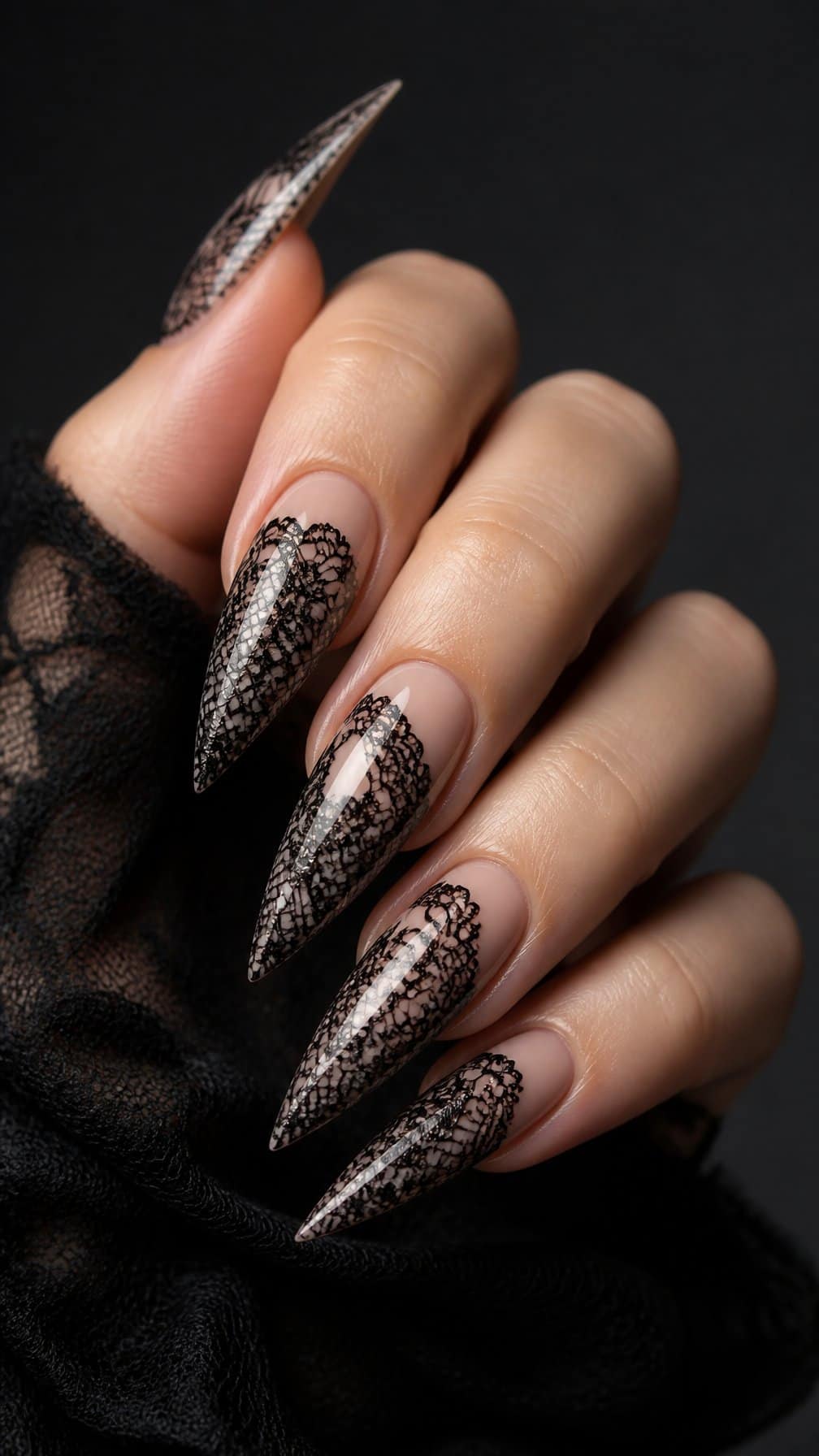 A hand displaying long pointed black lace-patterned nails.