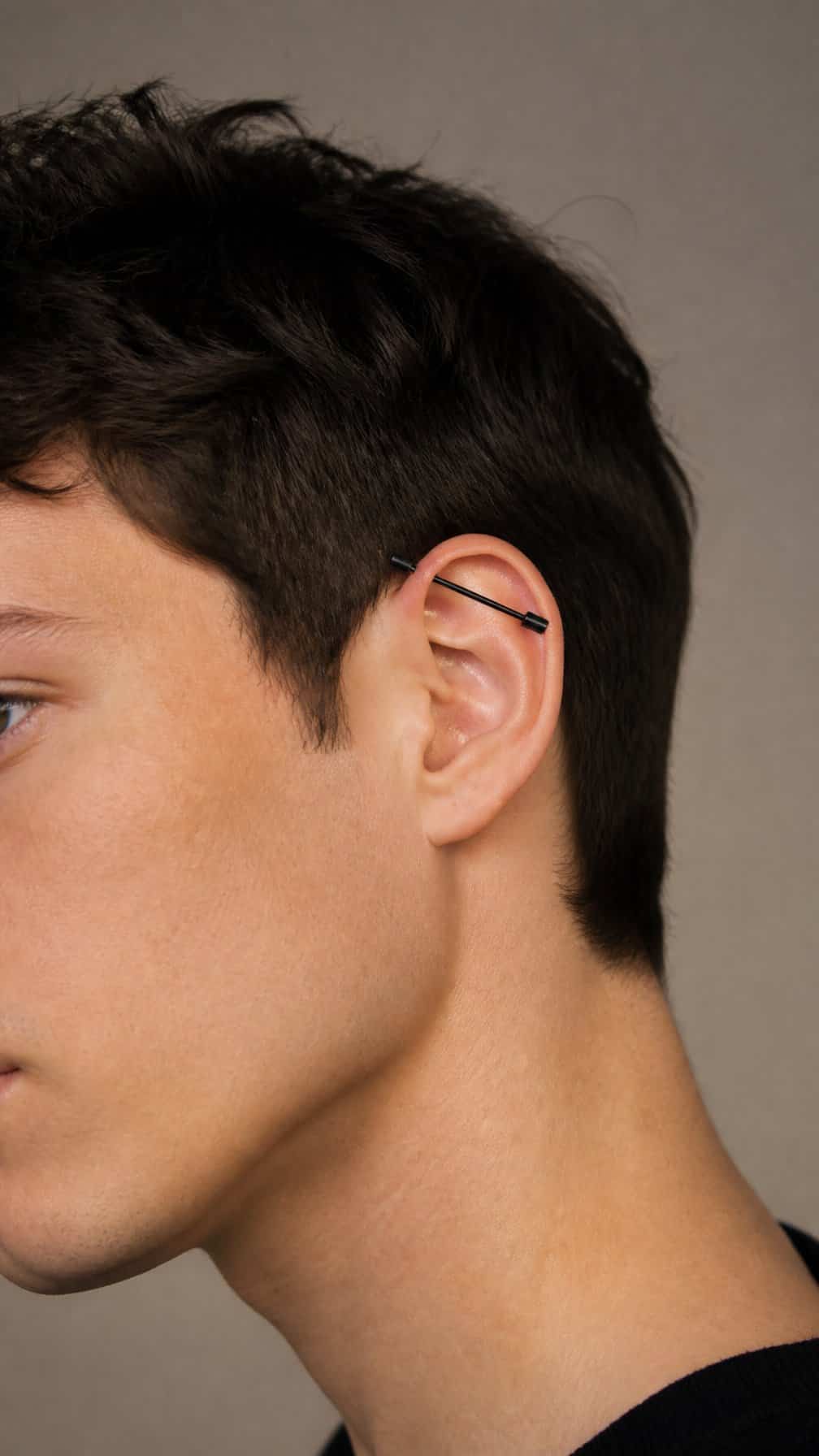 Close-up of an ear wearing a black industrial barbell piercing.