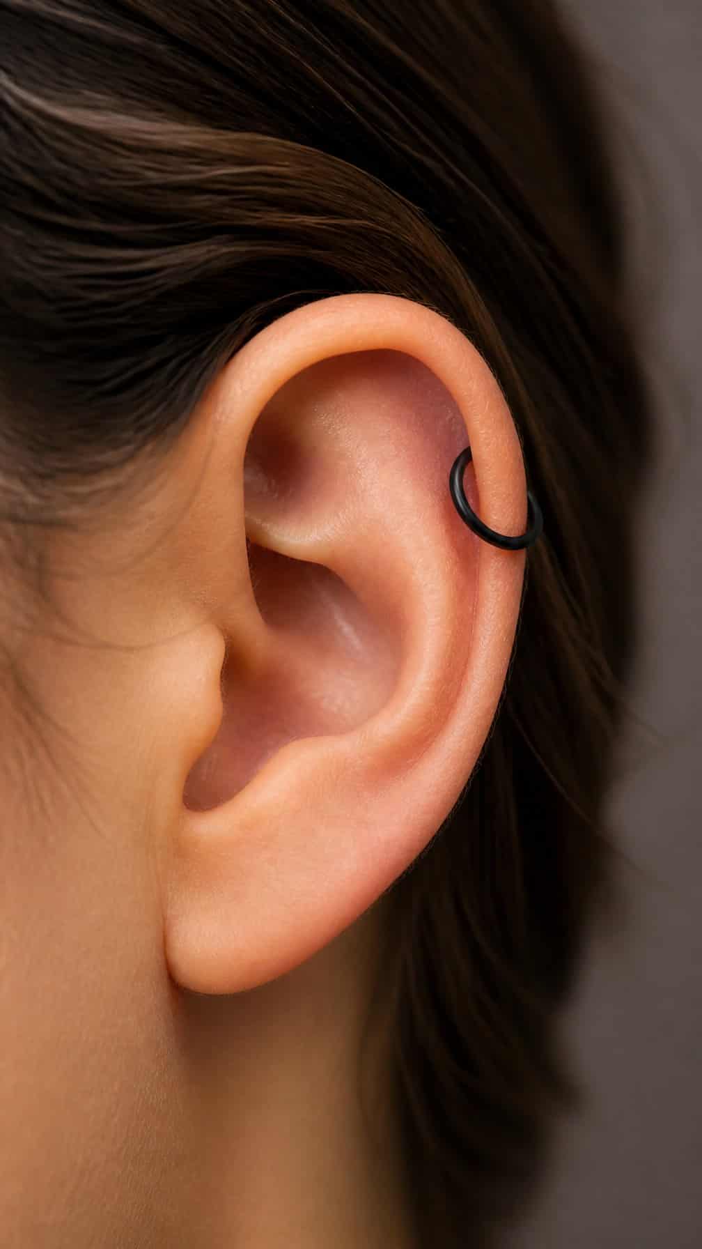 Close-up of an ear with a black titanium hoop piercing in the upper cartilage.