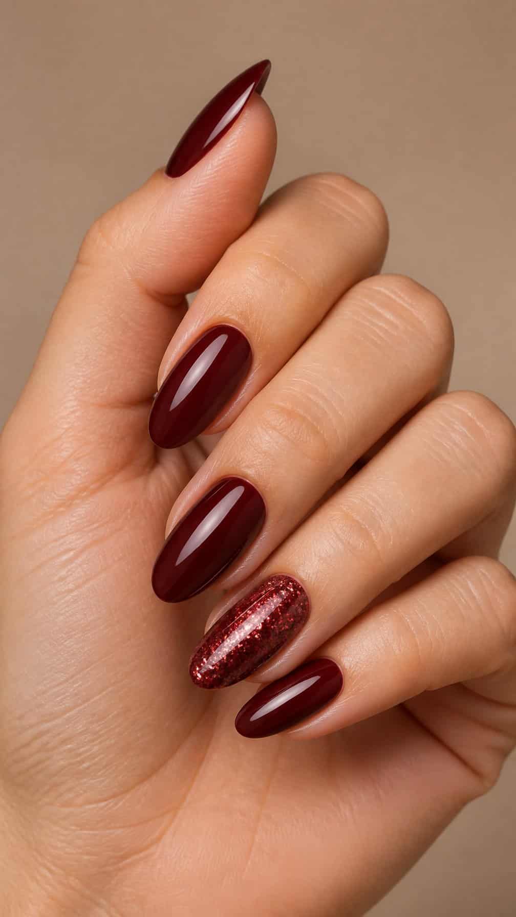 A hand with glossy burgundy nails and sparkling burgundy accent nails.