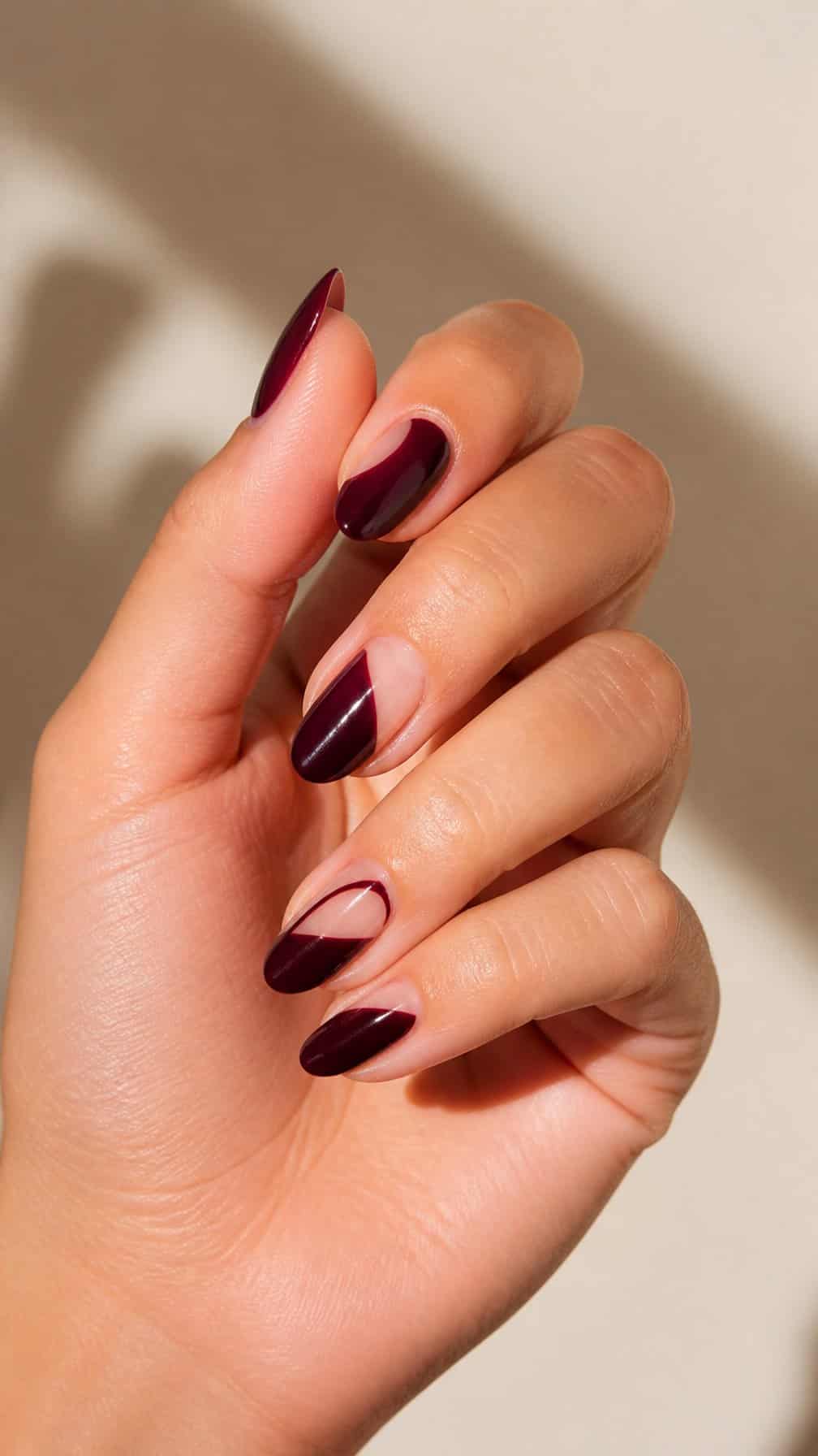 A hand with elegant burgundy negative-space nail art on almond-shaped nails.