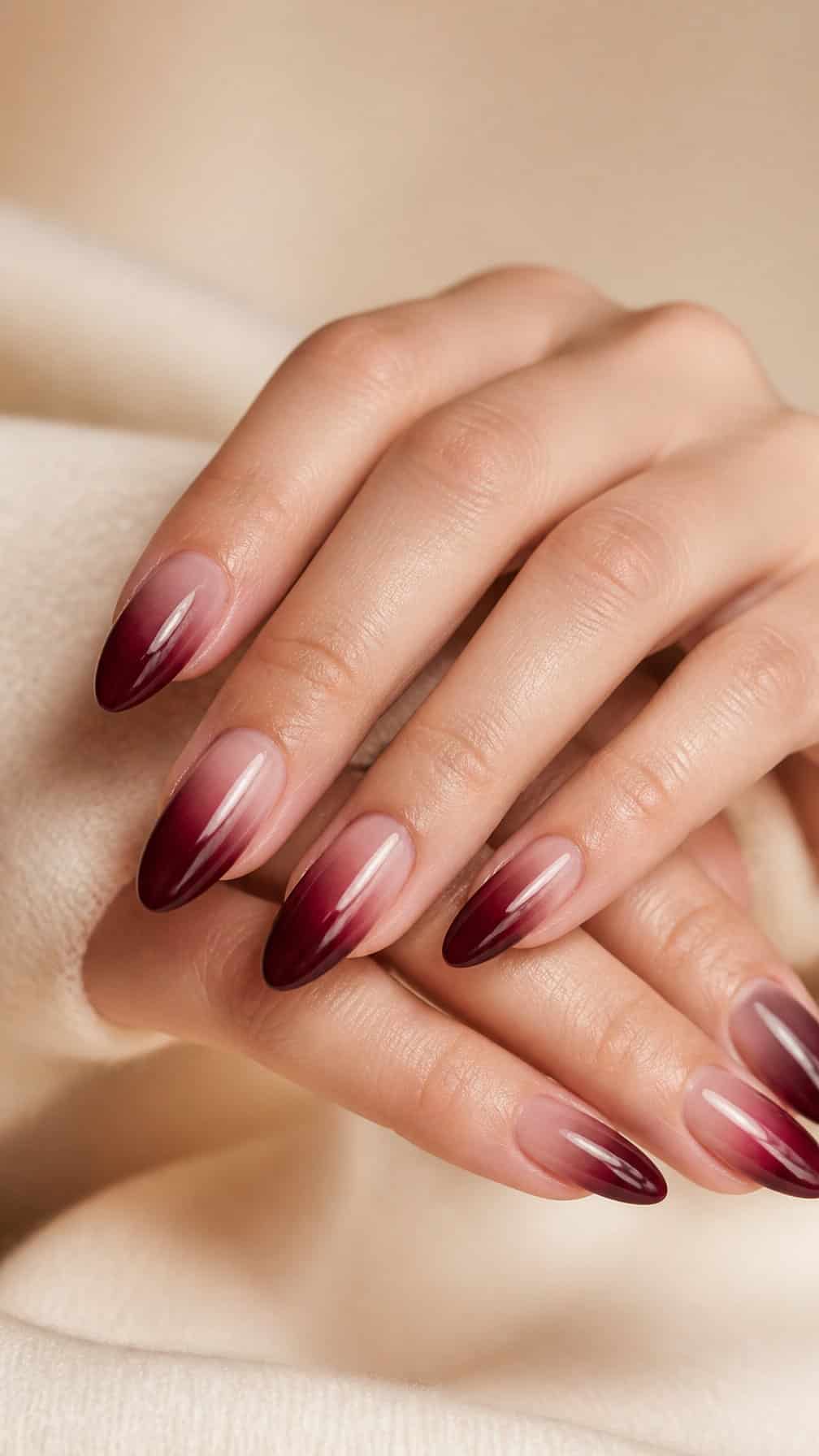 A close-up of hands with almond-shaped burgundy ombré manicured nails.