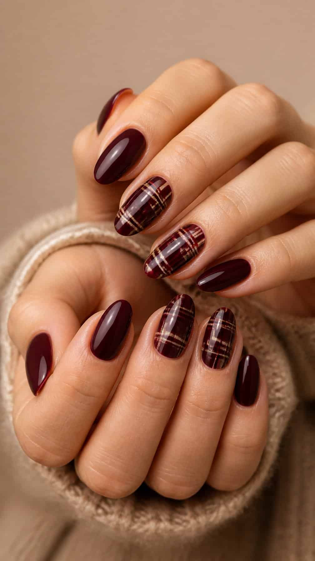 A close-up of hands with burgundy plaid and solid burgundy manicure.
