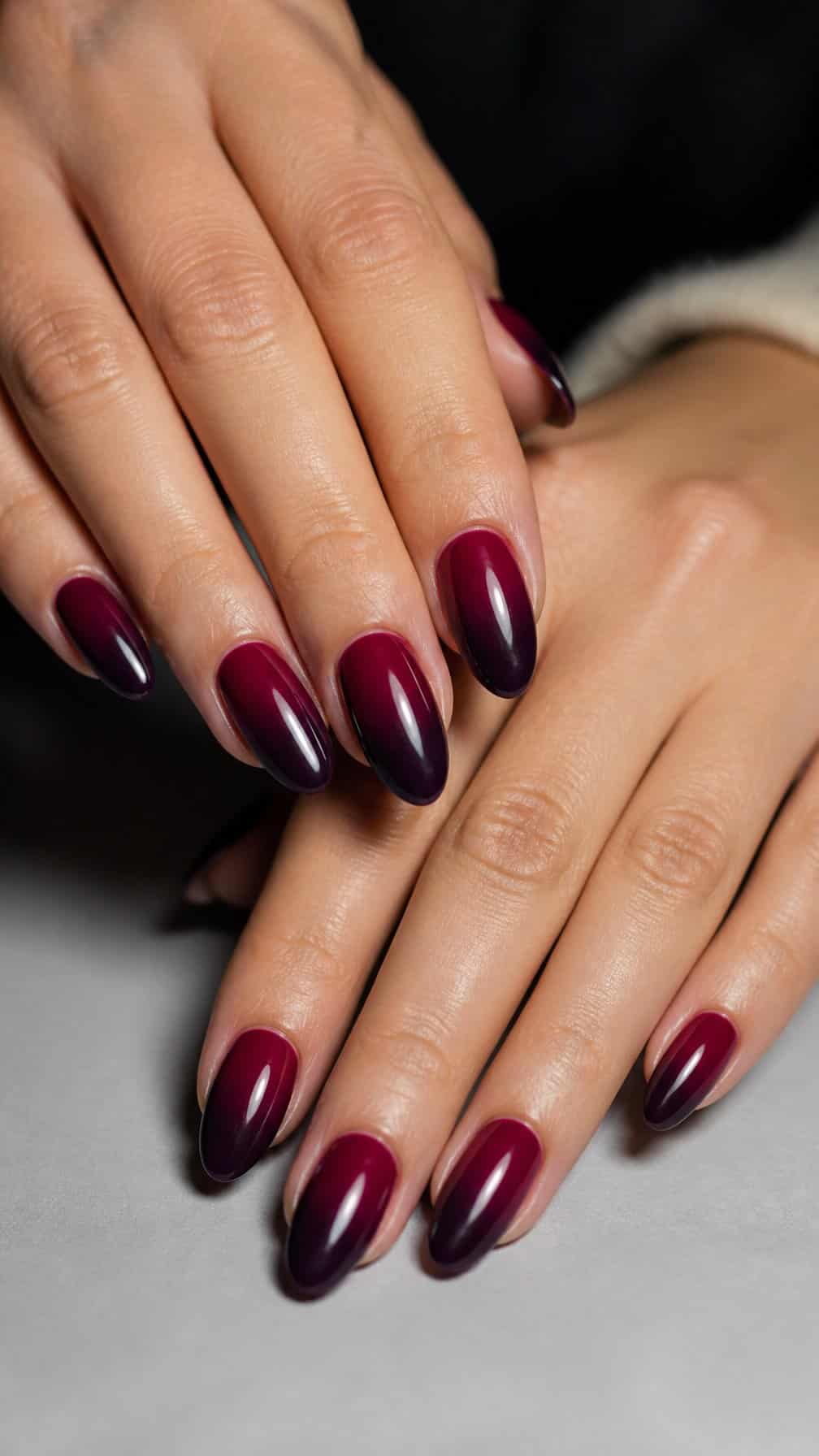 A close-up of a hand with glossy burgundy and plum ombre almond-shaped nails.