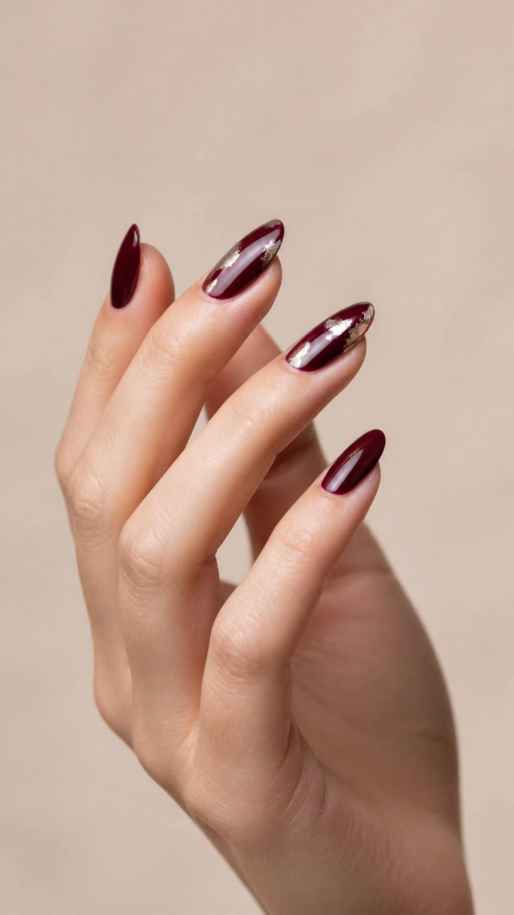 A manicured hand with glossy burgundy nails accented by silver foil details.