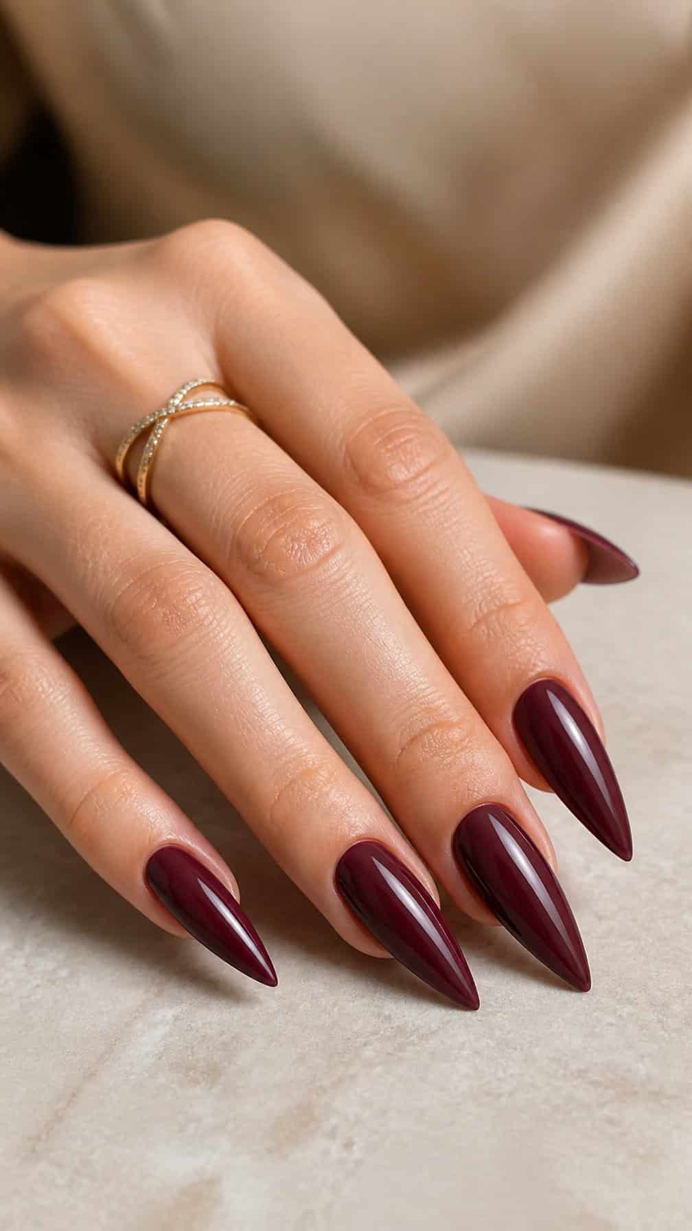 A hand with long glossy burgundy stiletto-shaped nails rests on a neutral surface.
