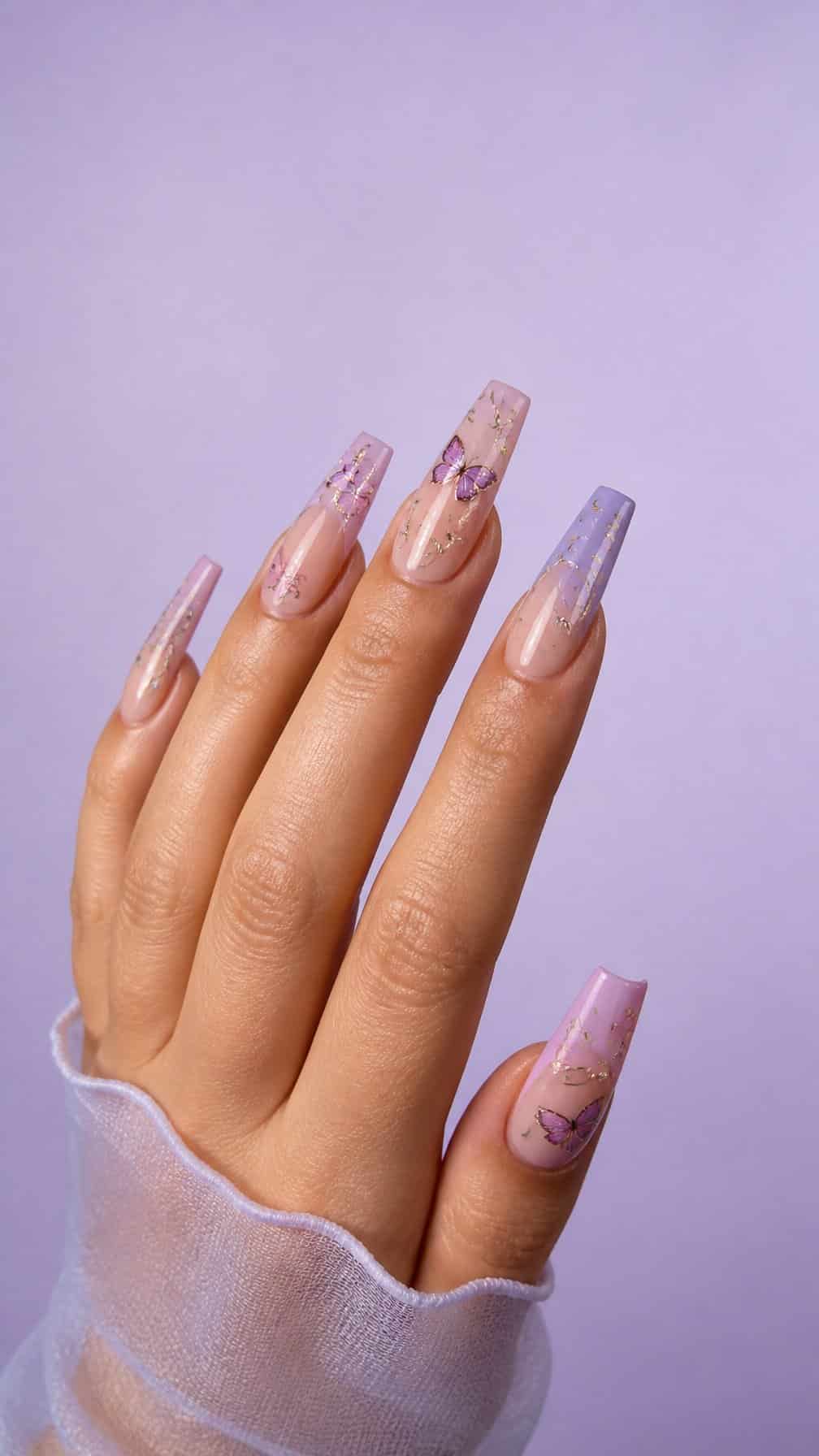 A hand displays long coffin-shaped nails decorated with pastel butterflies and small sparkling accents.