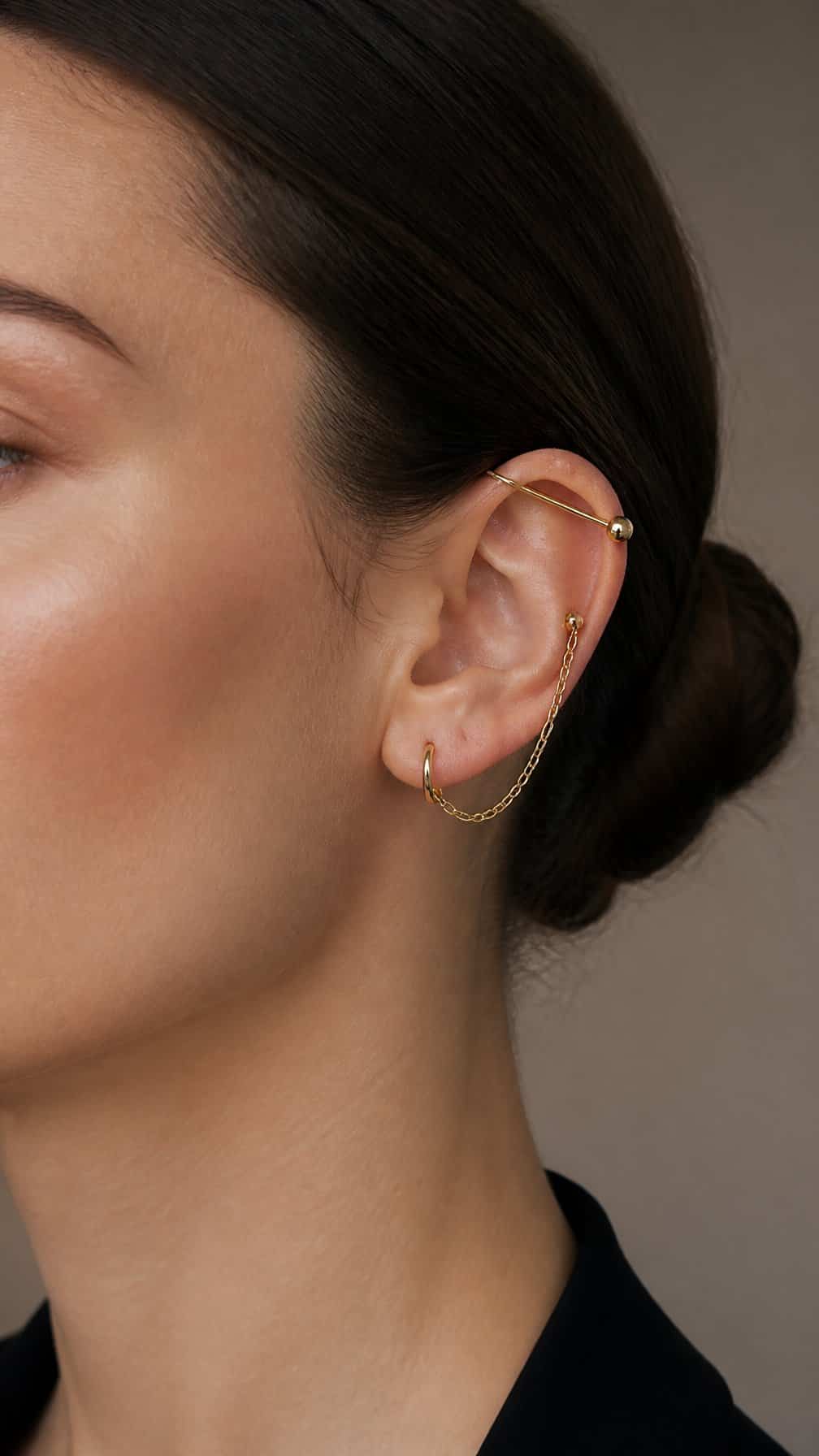Close-up of an ear wearing an industrial barbell and connected chain jewelry.