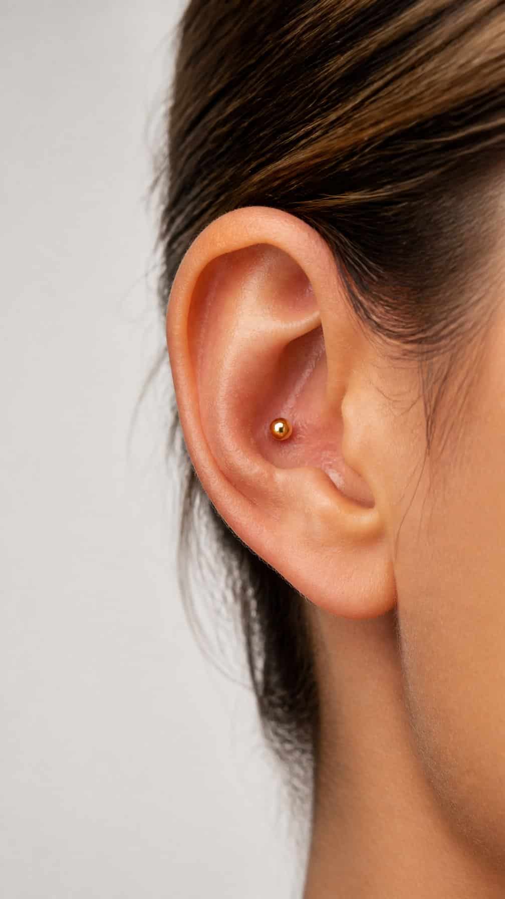 Close-up of an ear wearing a small gold ball conch stud.