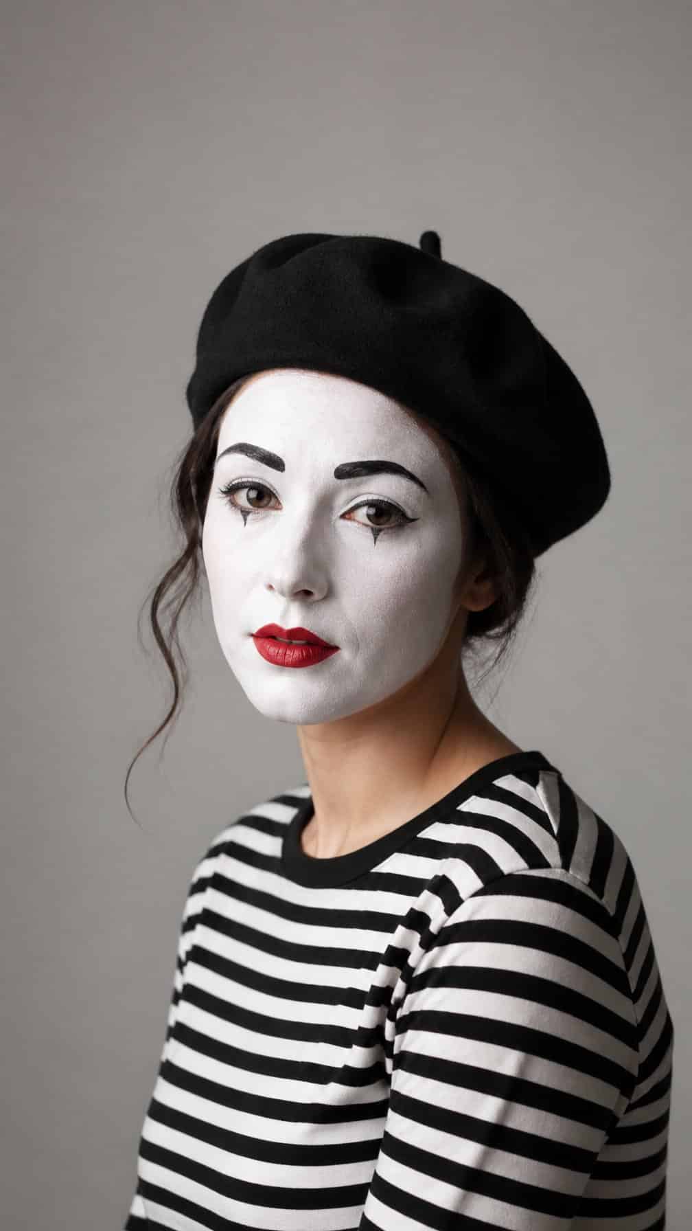 A person wearing classic mime makeup, a black beret, and a black-and-white striped shirt.
