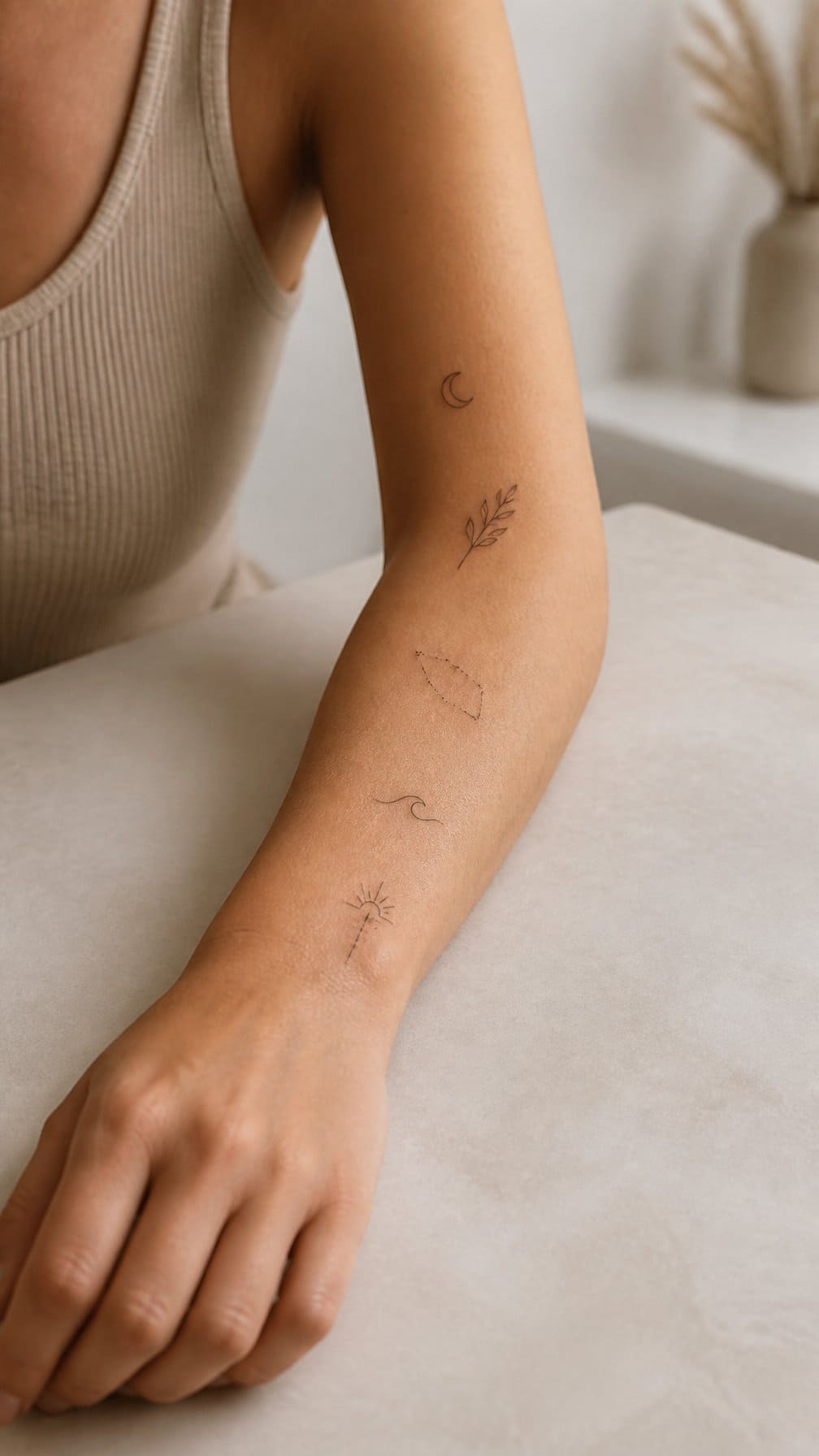 A close-up of a forearm with several small delicate tattoos resting on a neutral surface.
