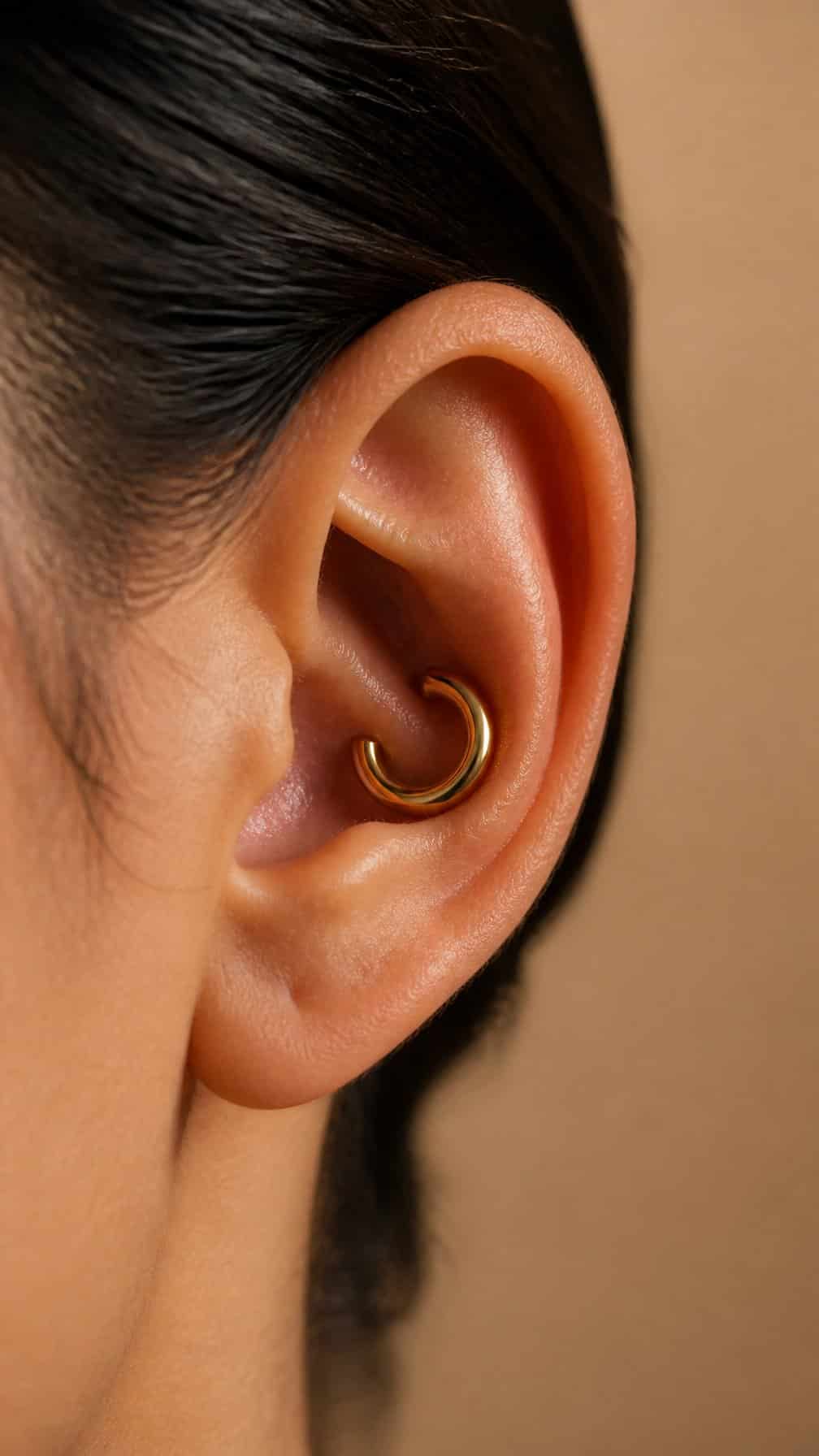 Close-up of an ear with a bold gold hoop in a conch piercing.