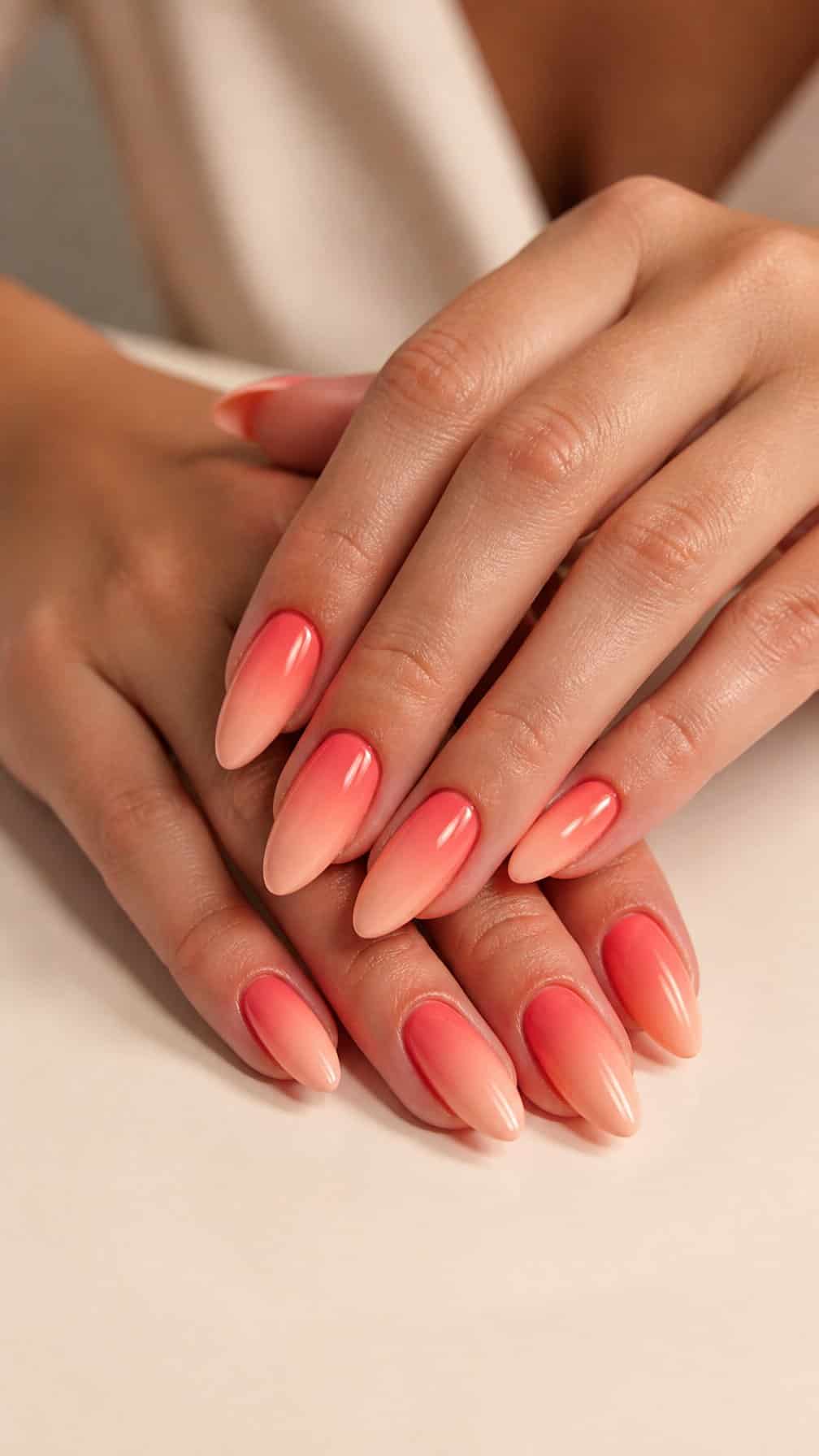 A close-up of almond-shaped nails with a glossy coral-to-peach gradient manicure.