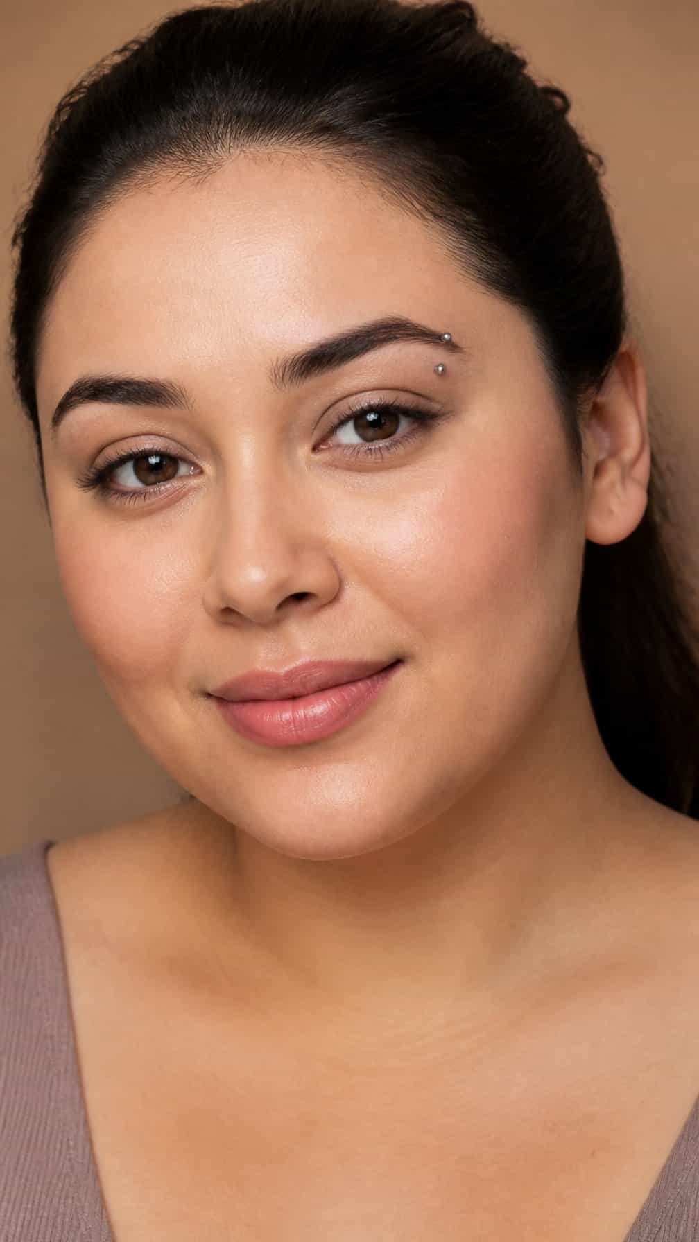 Close-up portrait of a person with a round face wearing a curved barbell eyebrow piercing.
