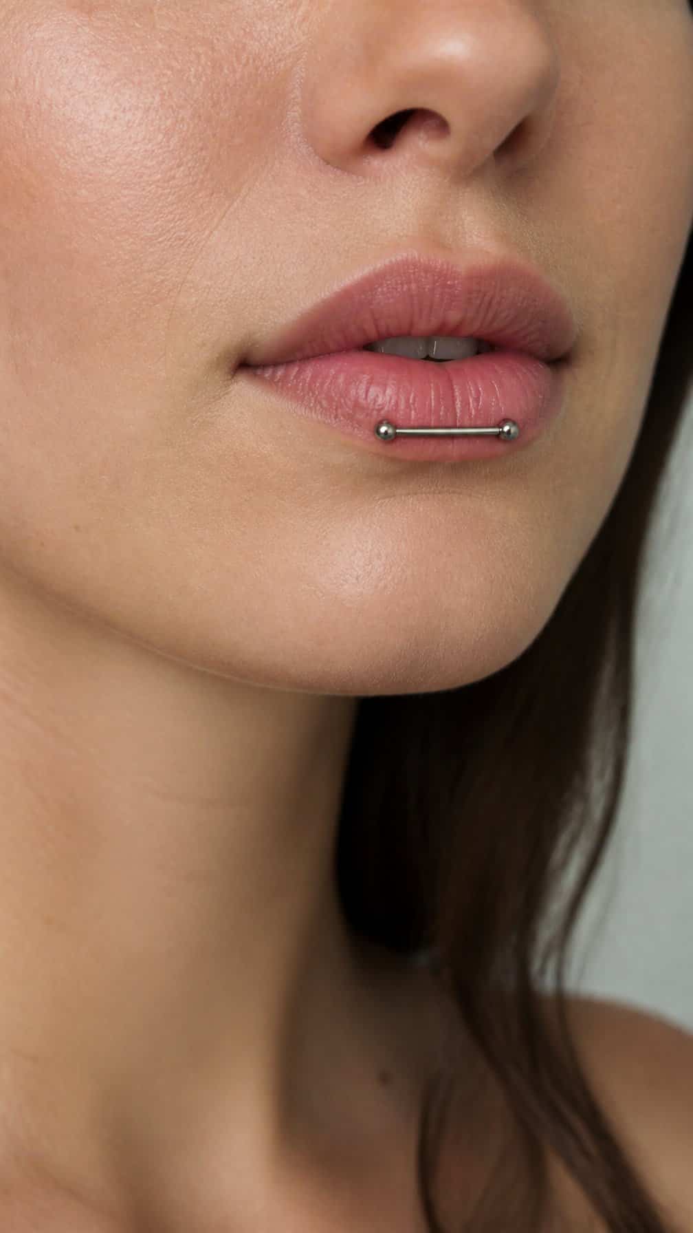 Close-up of a person showing a delicate horizontal piercing across the lower lip.