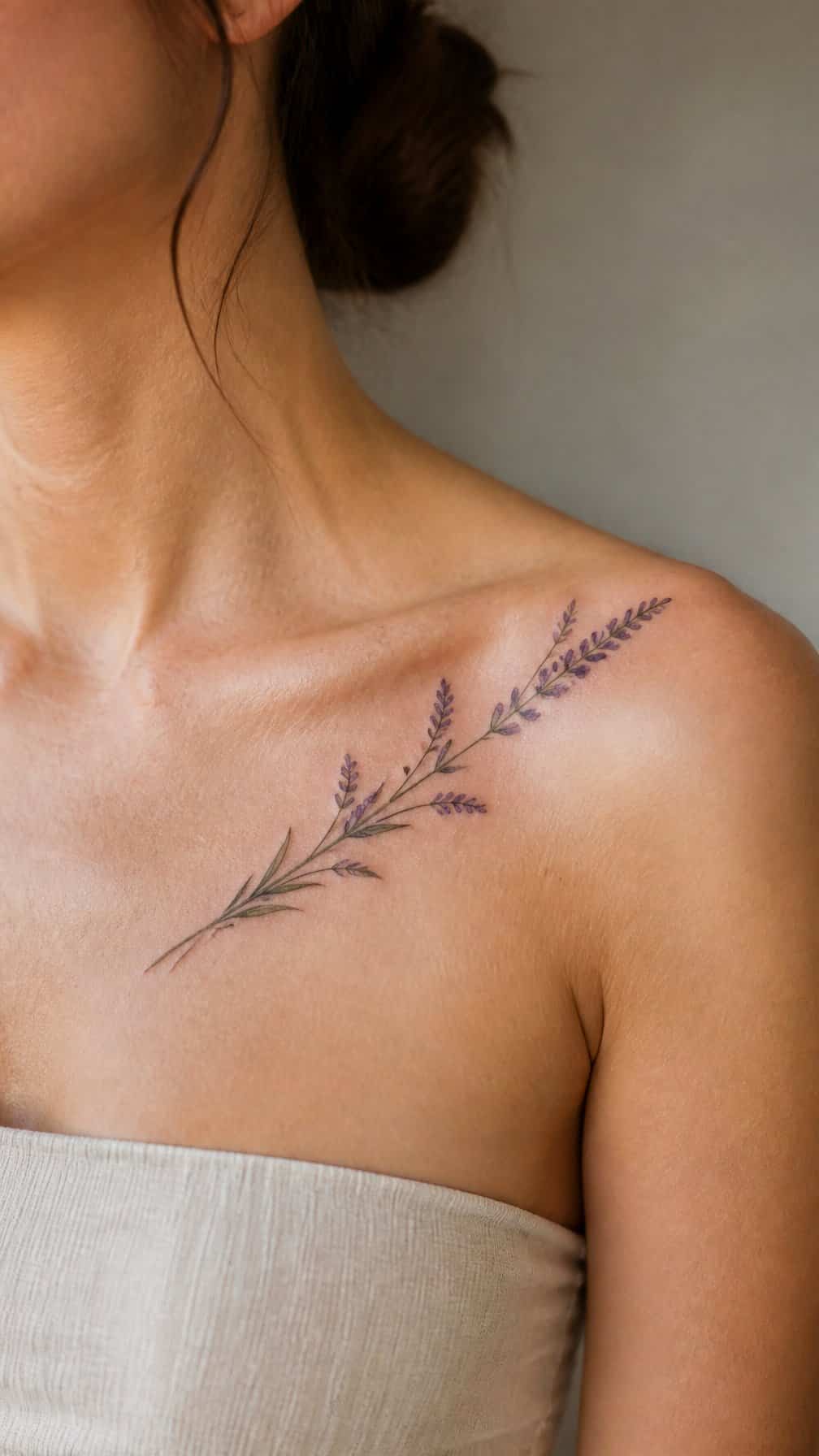 A lavender sprig tattoo follows the curve of a woman’s collarbone toward her shoulder.
