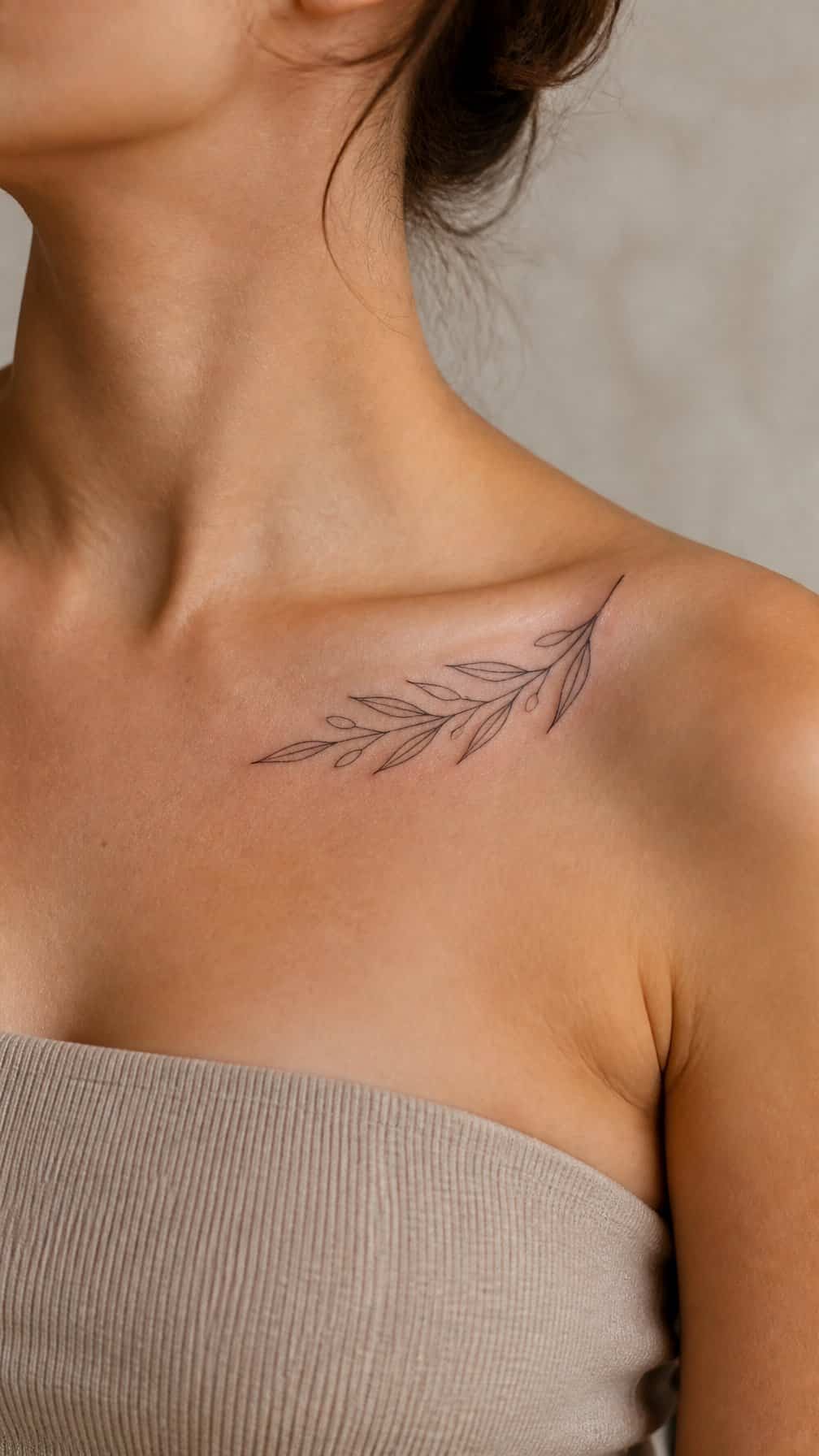 A delicate olive branch tattoo beneath an adult’s collarbone.