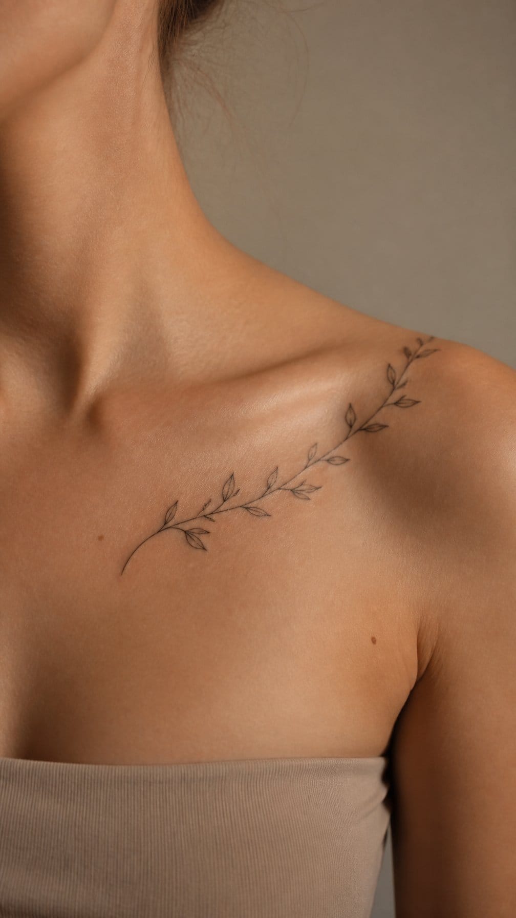 A delicate vine tattoo curves from an adult model’s collarbone toward the shoulder.