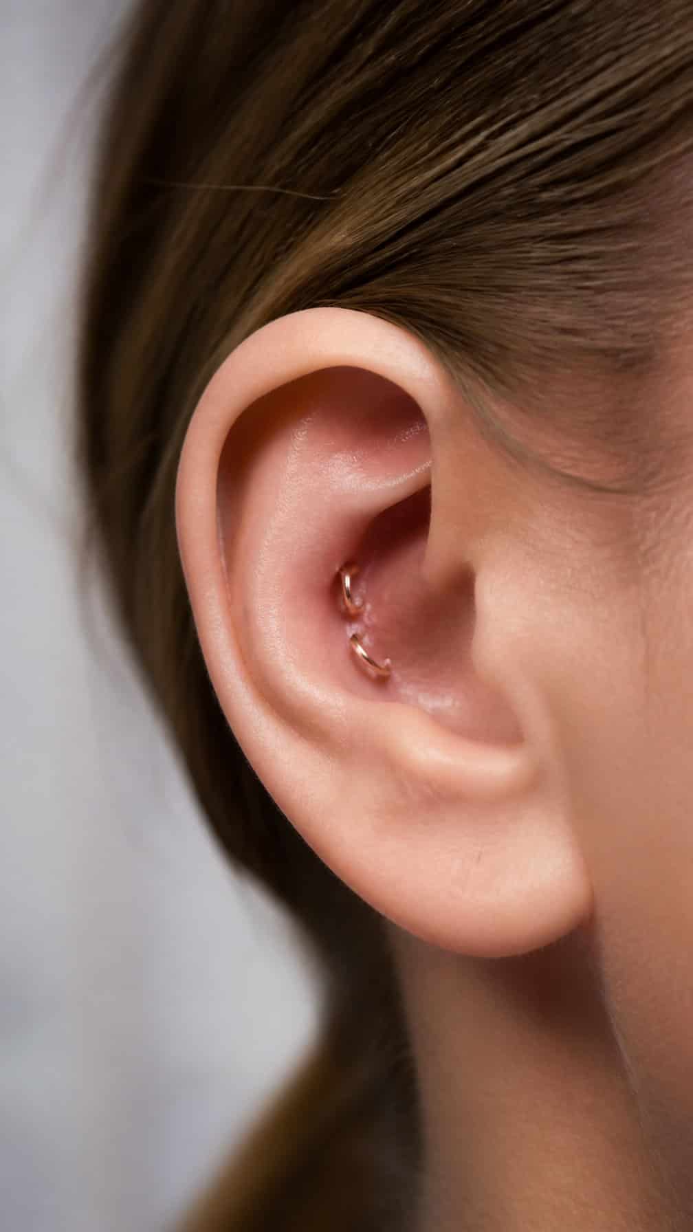 Close-up of an ear with two neatly stacked conch piercings wearing delicate jewelry.
