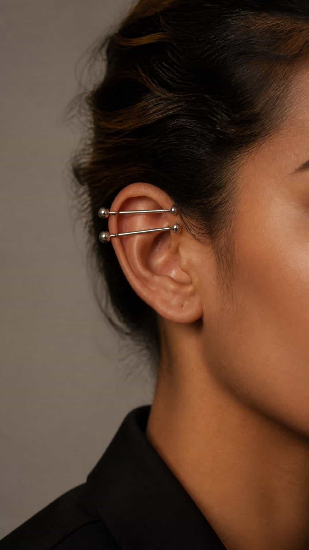 Close-up of an ear featuring two coordinated industrial piercings through the upper cartilage.
