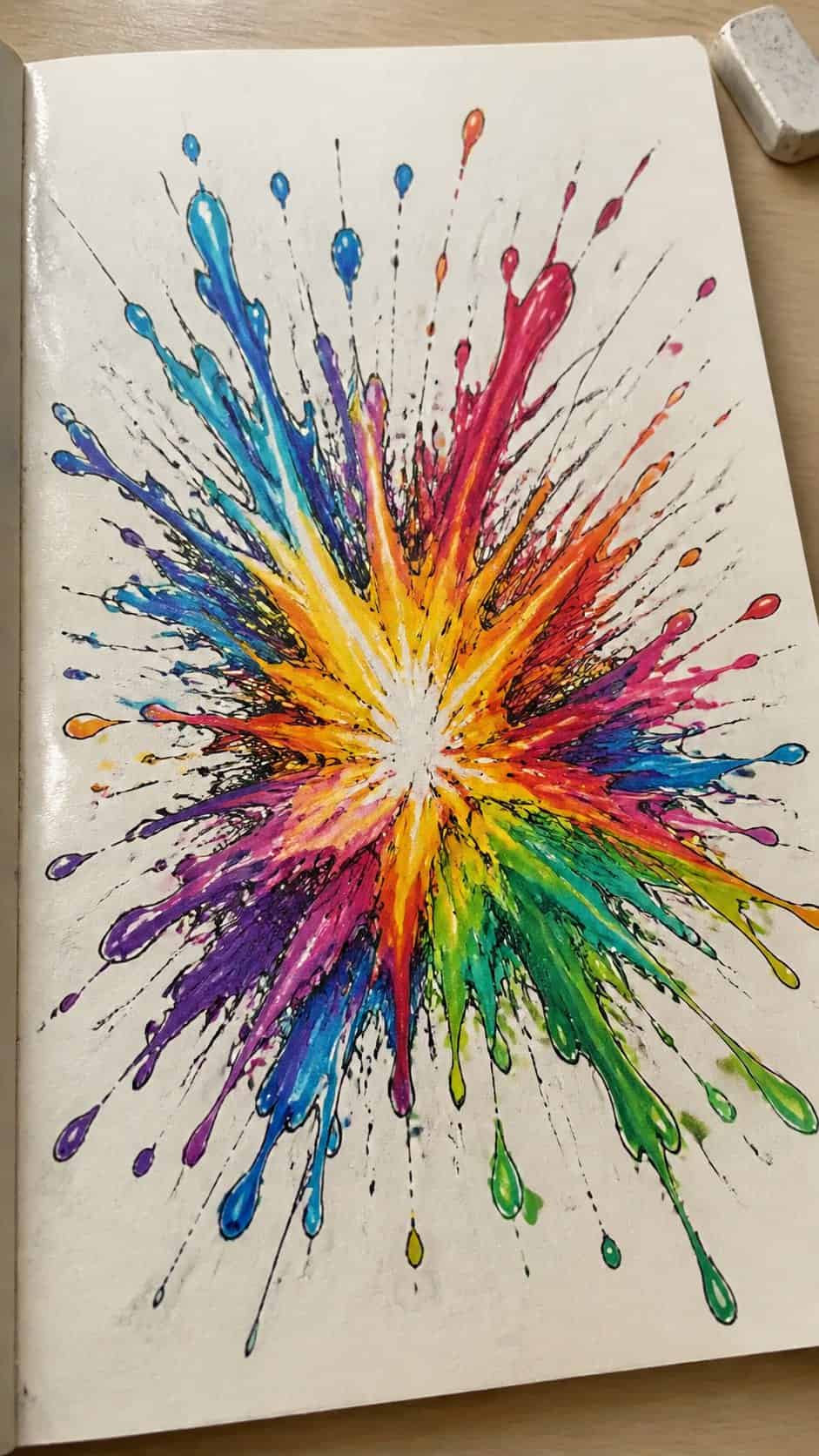Hand-drawn color splash explosion in marker drawing on textured paper, shown in a gentle oblique desk view that shows paper tooth and — study 2