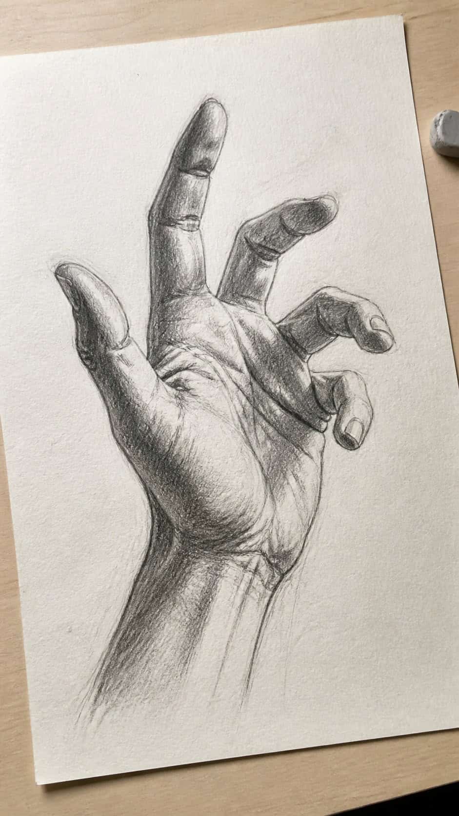 Hand-drawn expressive hand gestures in graphite drawing on textured paper, shown in a gentle oblique desk view that shows paper tooth — study 1
