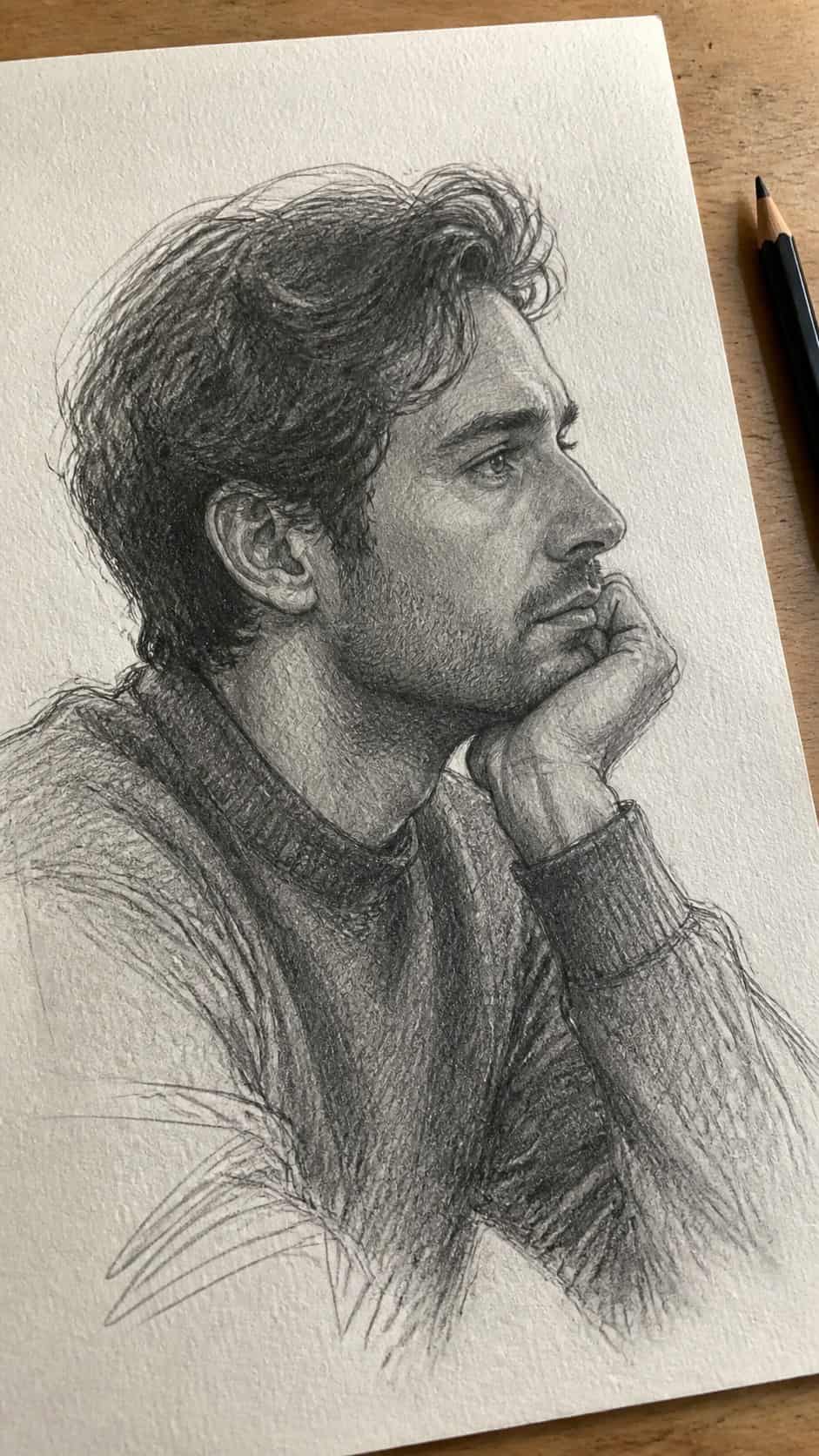 Hand-drawn pensive profile in graphite drawing on textured paper, shown in a gentle oblique desk view that shows paper tooth and — study 2