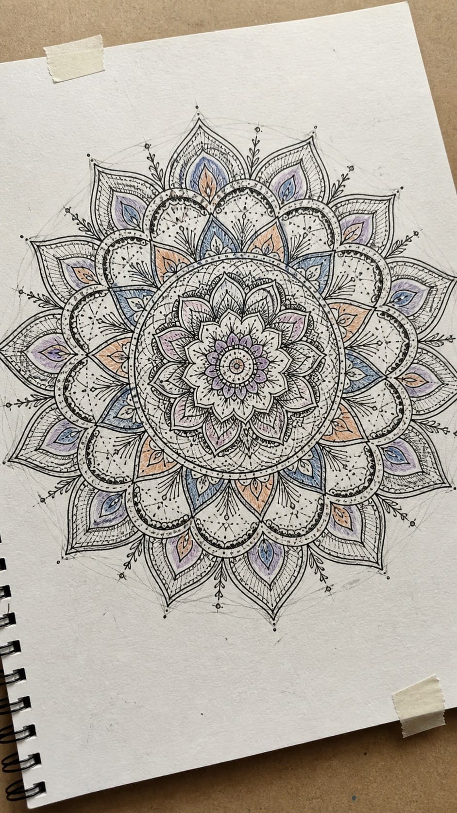 Hand-drawn intricate mandalas in ink and colored-pencil drawing on textured paper, shown in a gentle oblique desk view that shows — study 2