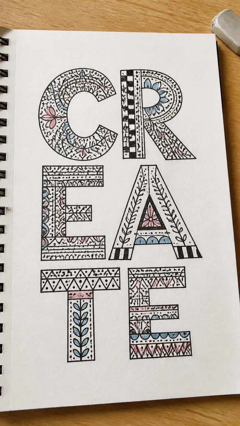 Hand-drawn doodle letters in ink and colored-pencil drawing on textured paper, shown in a close overhead crop — study 2