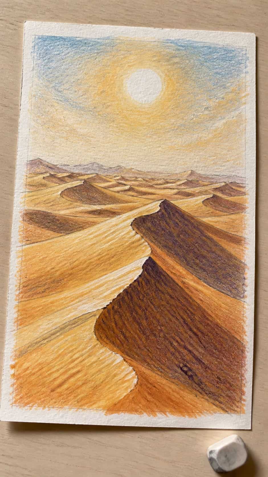 Hand-drawn desert dunes in colored-pencil and gouache drawing on textured paper, shown in a gentle oblique desk view that shows paper — study 2