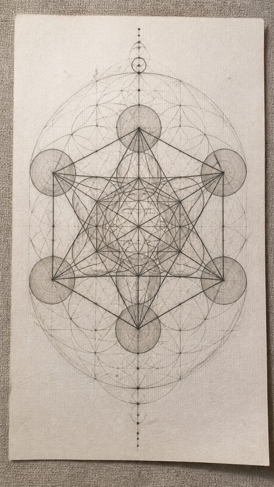 Hand-drawn sacred geometry in graphite drawing on textured paper, shown in a slightly off-center overhead composition, like an artist — study 1