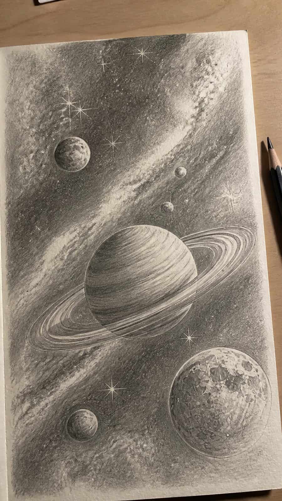 Hand-drawn celestial bodies in graphite drawing on textured paper, shown in a slightly off-center overhead composition, like an artist — study 2