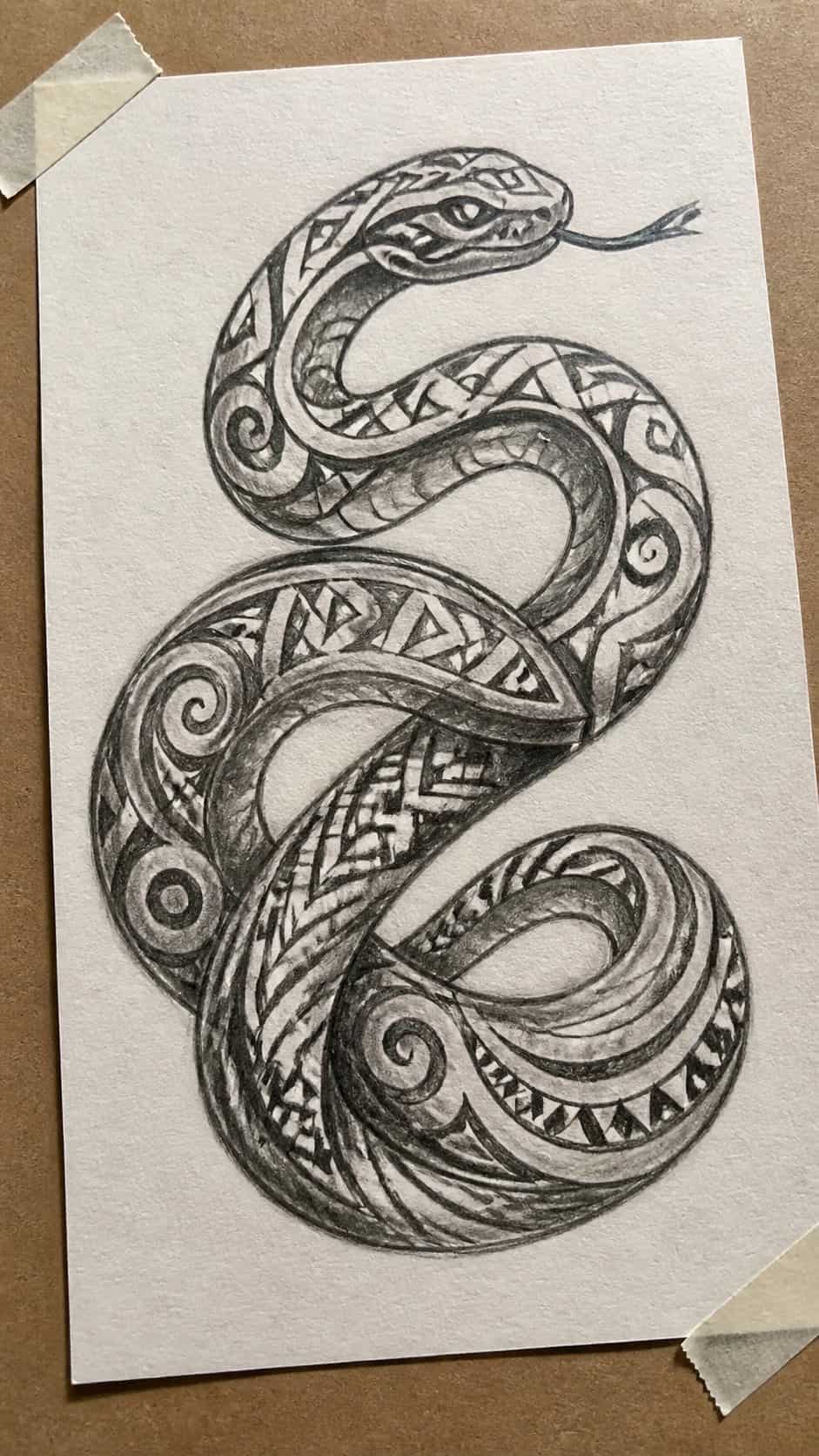 Hand-drawn serpentine tribal art in graphite drawing on textured paper, shown in a gentle oblique desk view that shows paper tooth and — study 1