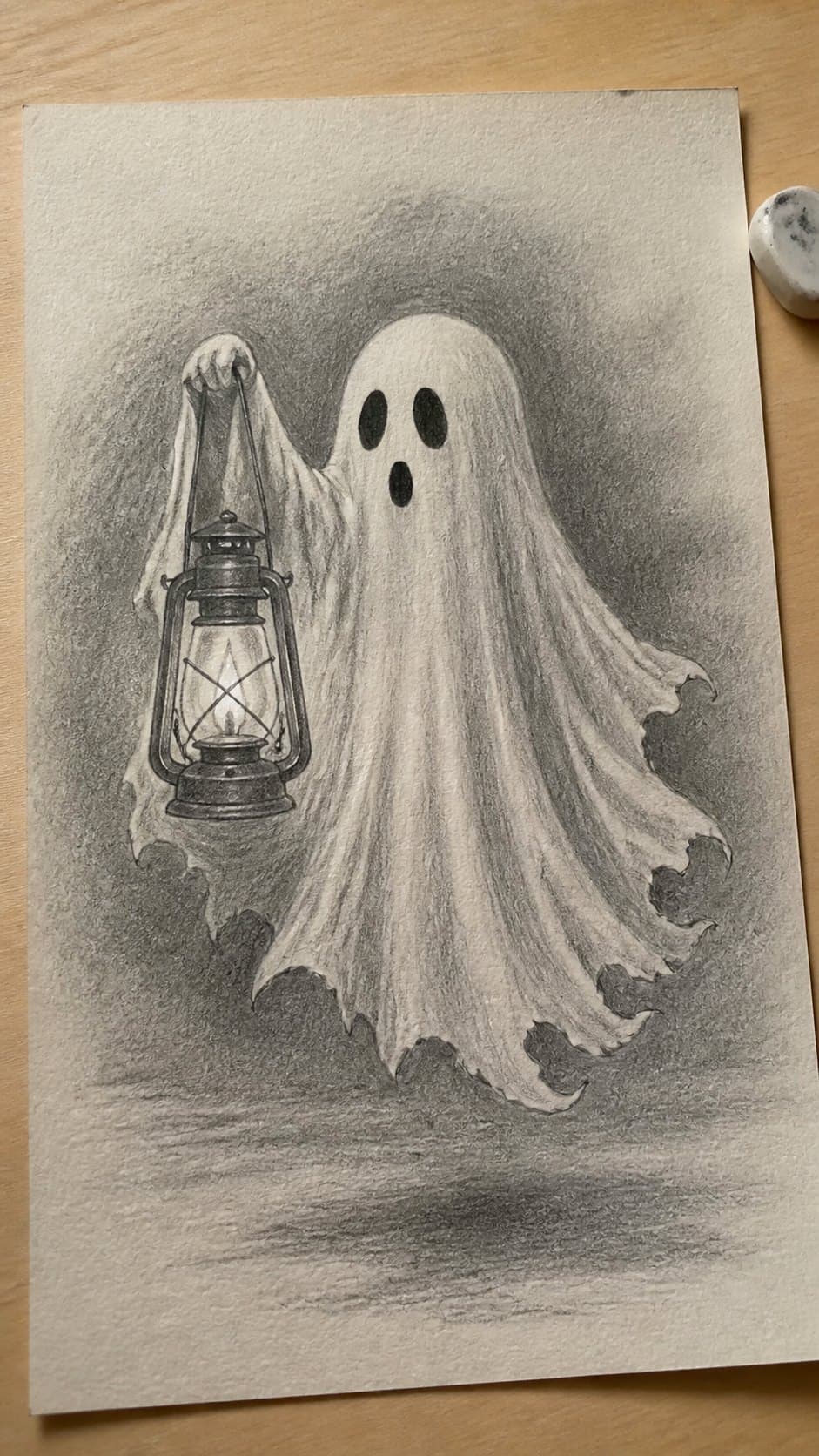 18 Ghost Drawing Ideas for Spooky and Expressive Sketches 5 Hand-drawn ghost holding a lantern in graphite drawing on textured paper, shown in a gentle oblique desk view that shows paper tooth — study 1