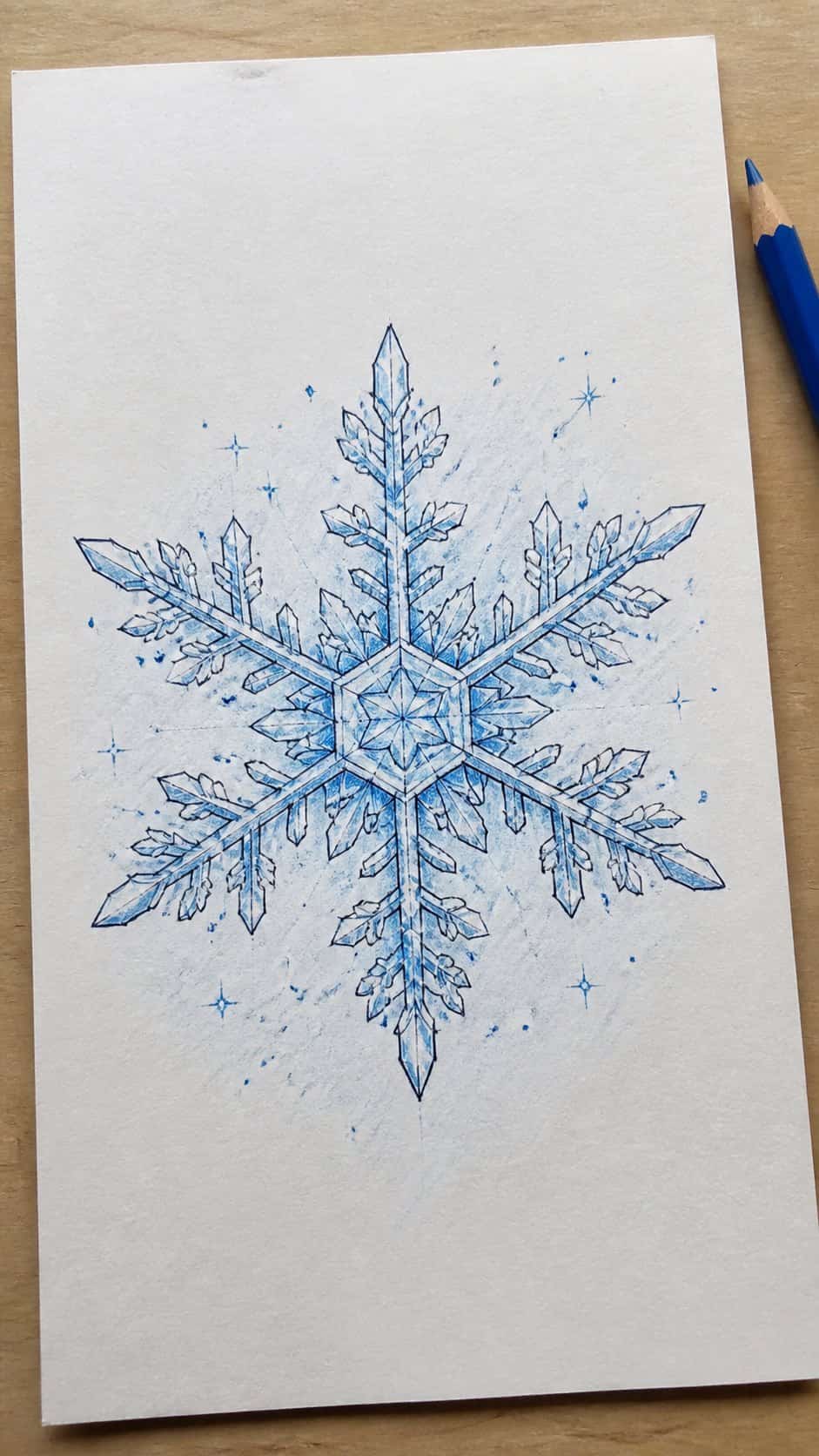Hand-drawn snowflake in colored-pencil drawing on textured paper, shown in a slightly off-center overhead composition, like an artist — study 1