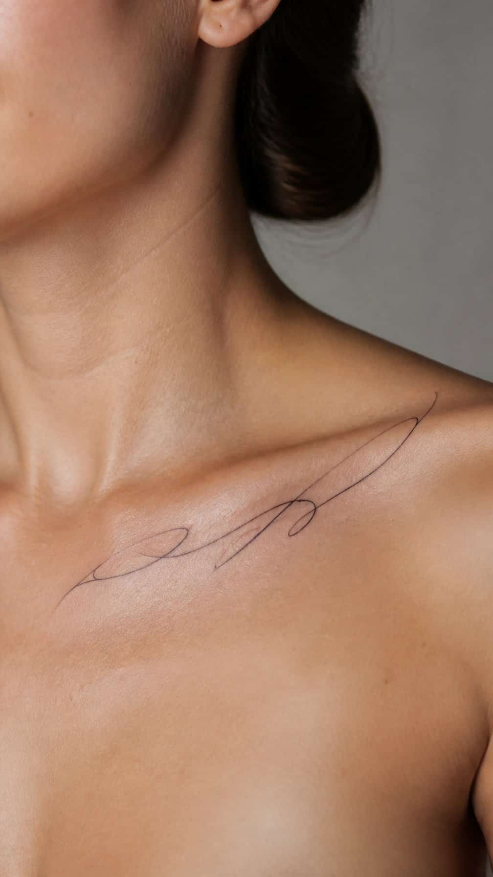 Close-up of a person with a delicate flowing tattoo along the collarbone.