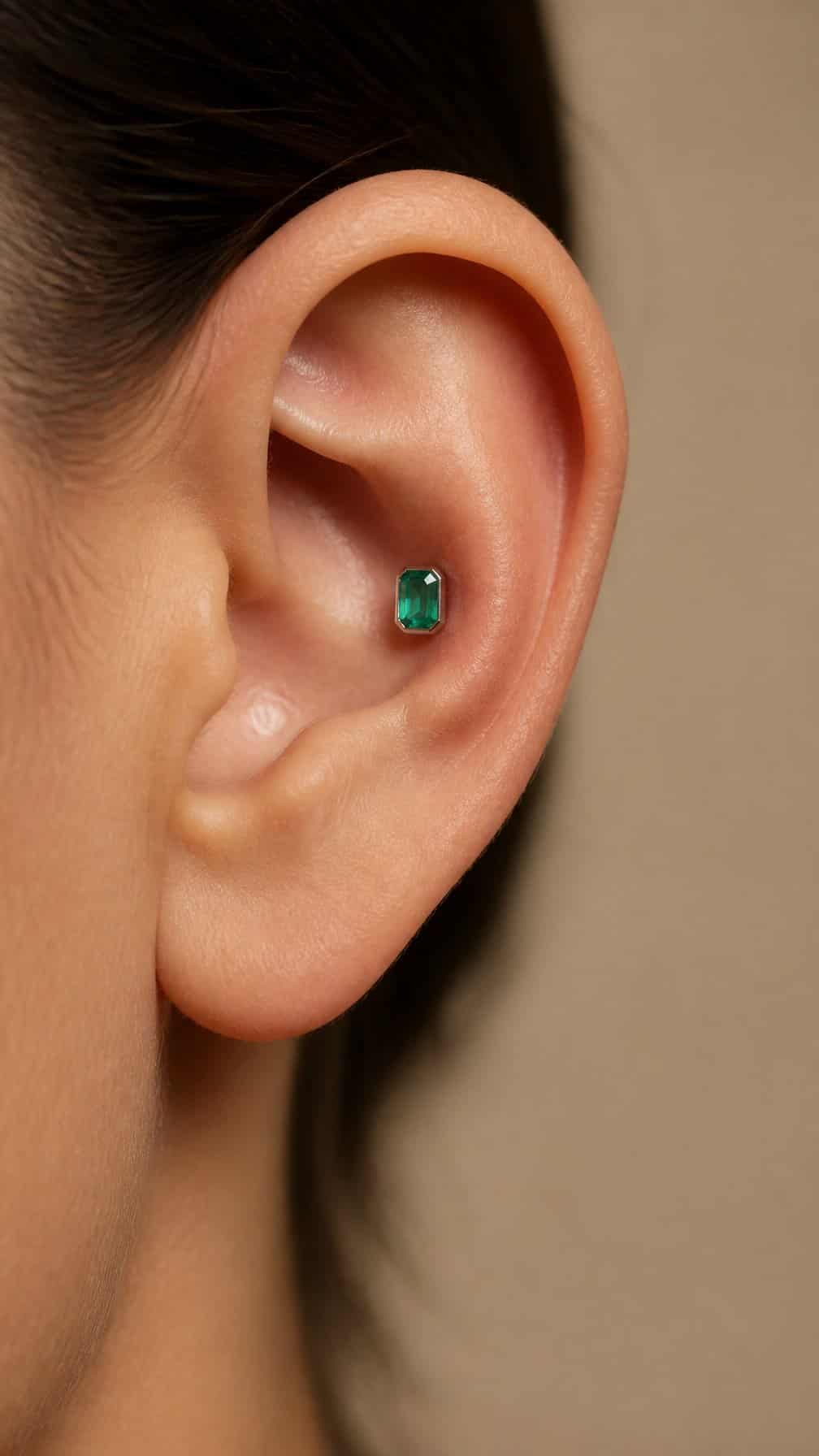 Close-up of an ear with a green emerald-cut gemstone conch stud.