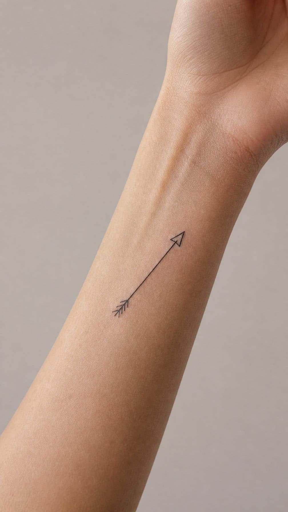A close-up of a forearm with a small arrow tattoo.