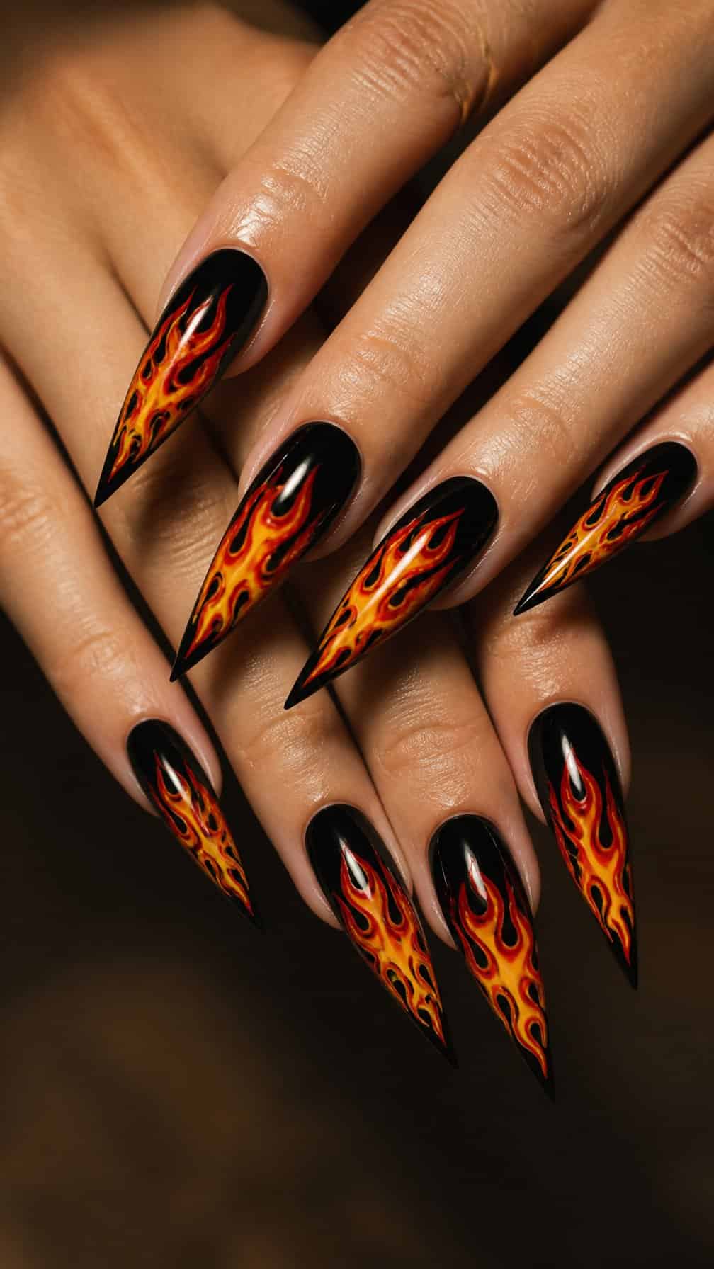 A close-up of two hands with long pointed nails painted with colorful flame designs.