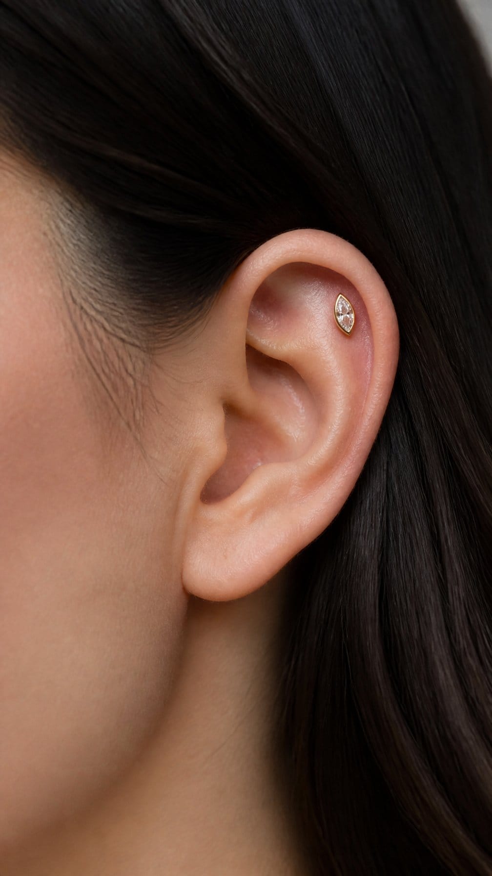 Close-up of an ear with a marquise gemstone flat piercing on the upper cartilage.
