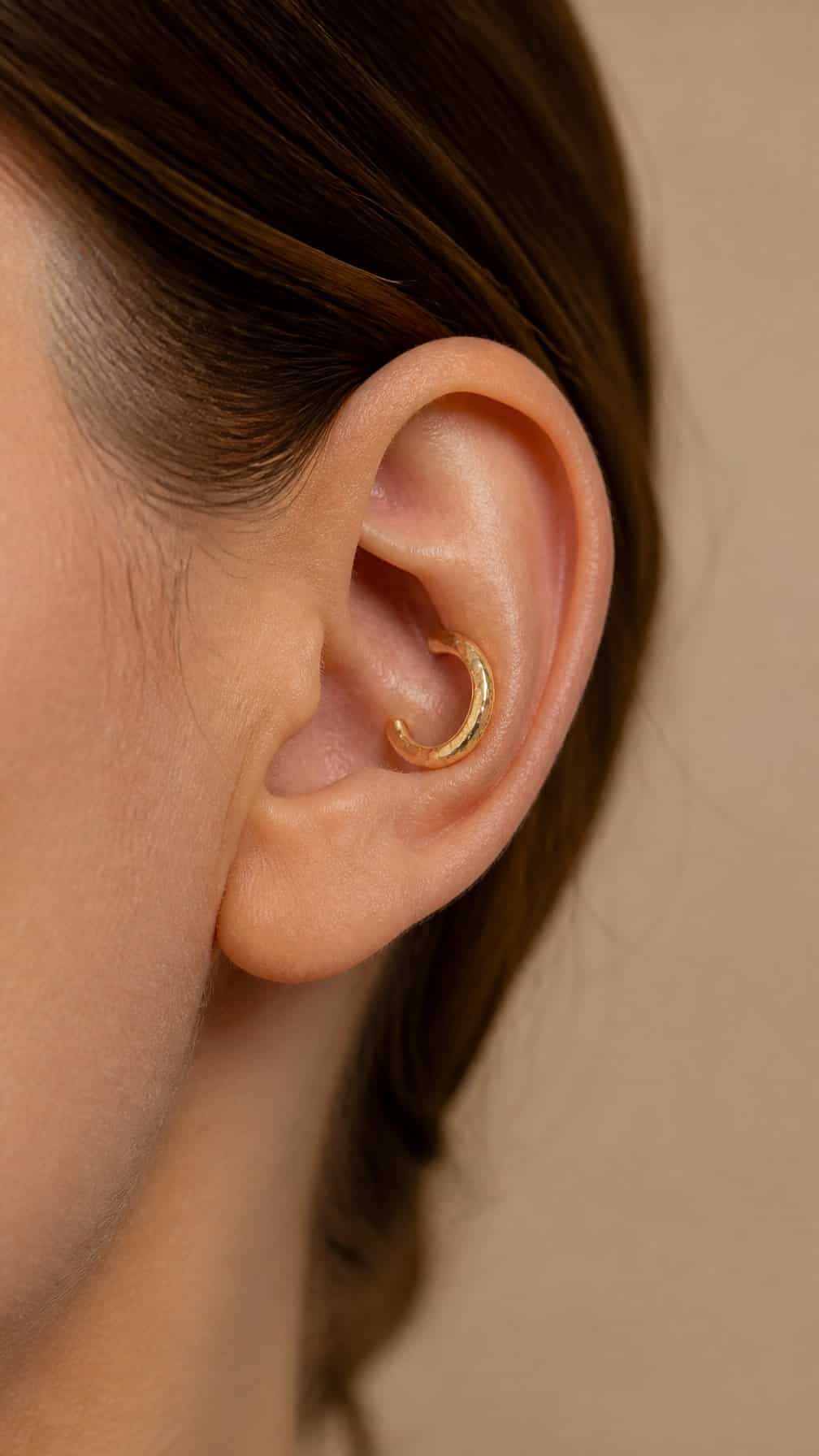 Close-up of an ear wearing a hammered gold hoop in the conch piercing.
