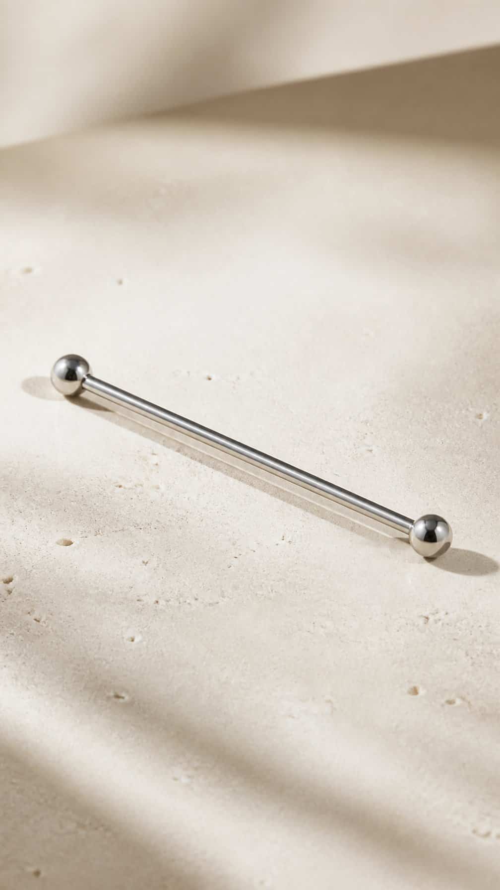 A minimalist industrial barbell earring resting on a neutral surface.