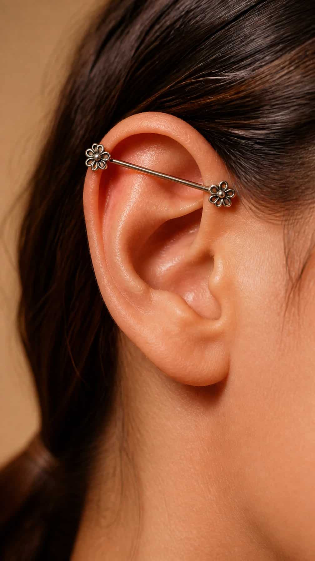 Close-up of an ear wearing an industrial piercing with floral-shaped ends.