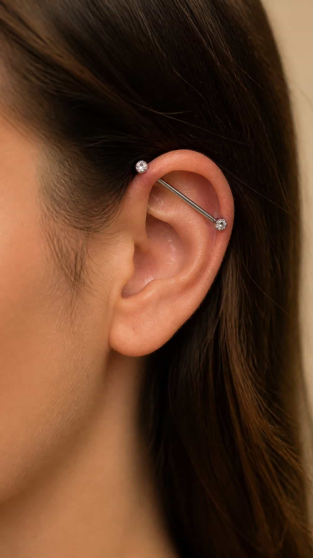 Close-up of an ear with a diagonal industrial barbell piercing featuring small gemstone ends.