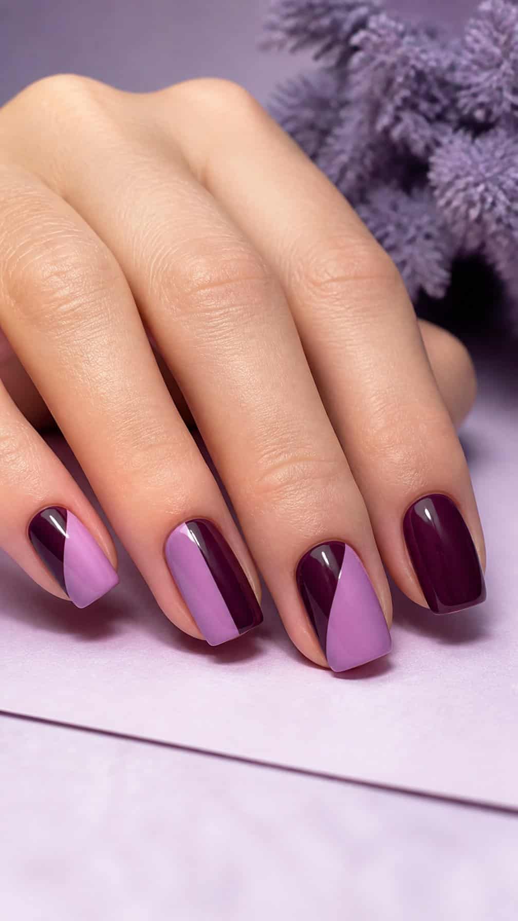A hand with neatly manicured nails painted in lavender and deep plum geometric blocks.