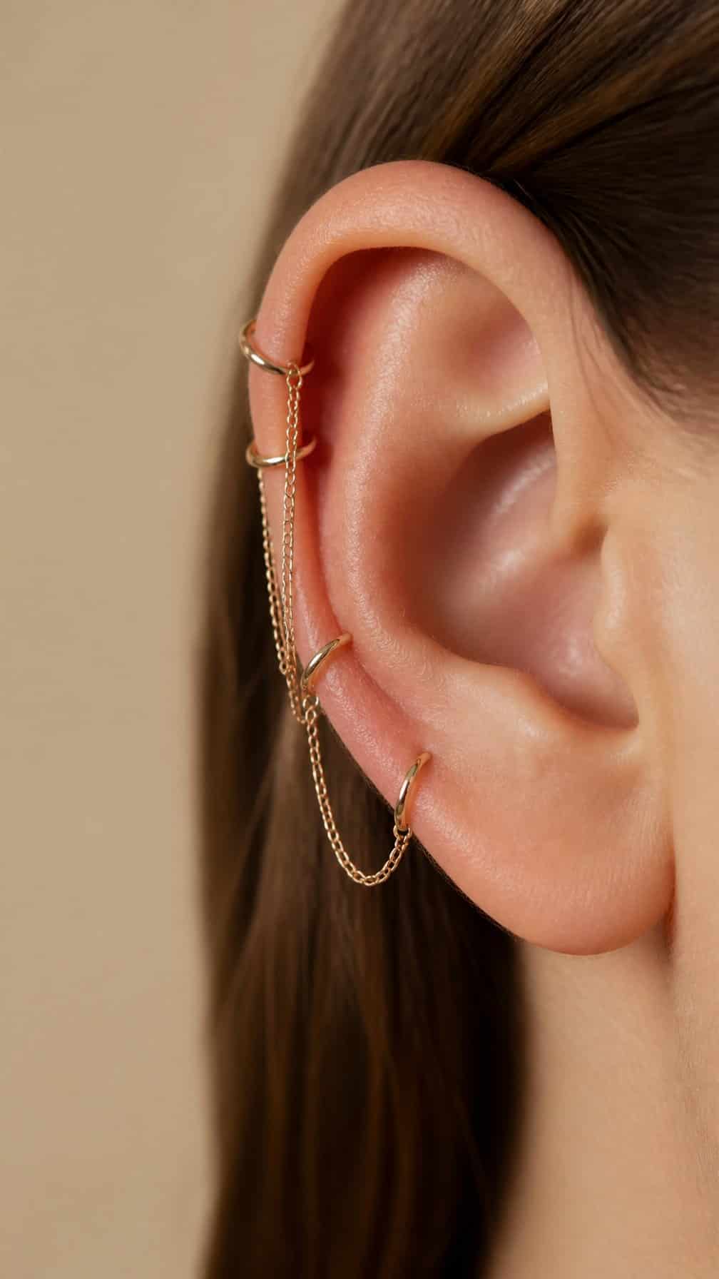 Close-up of an ear with layered chain and hoop piercings along the upper cartilage.