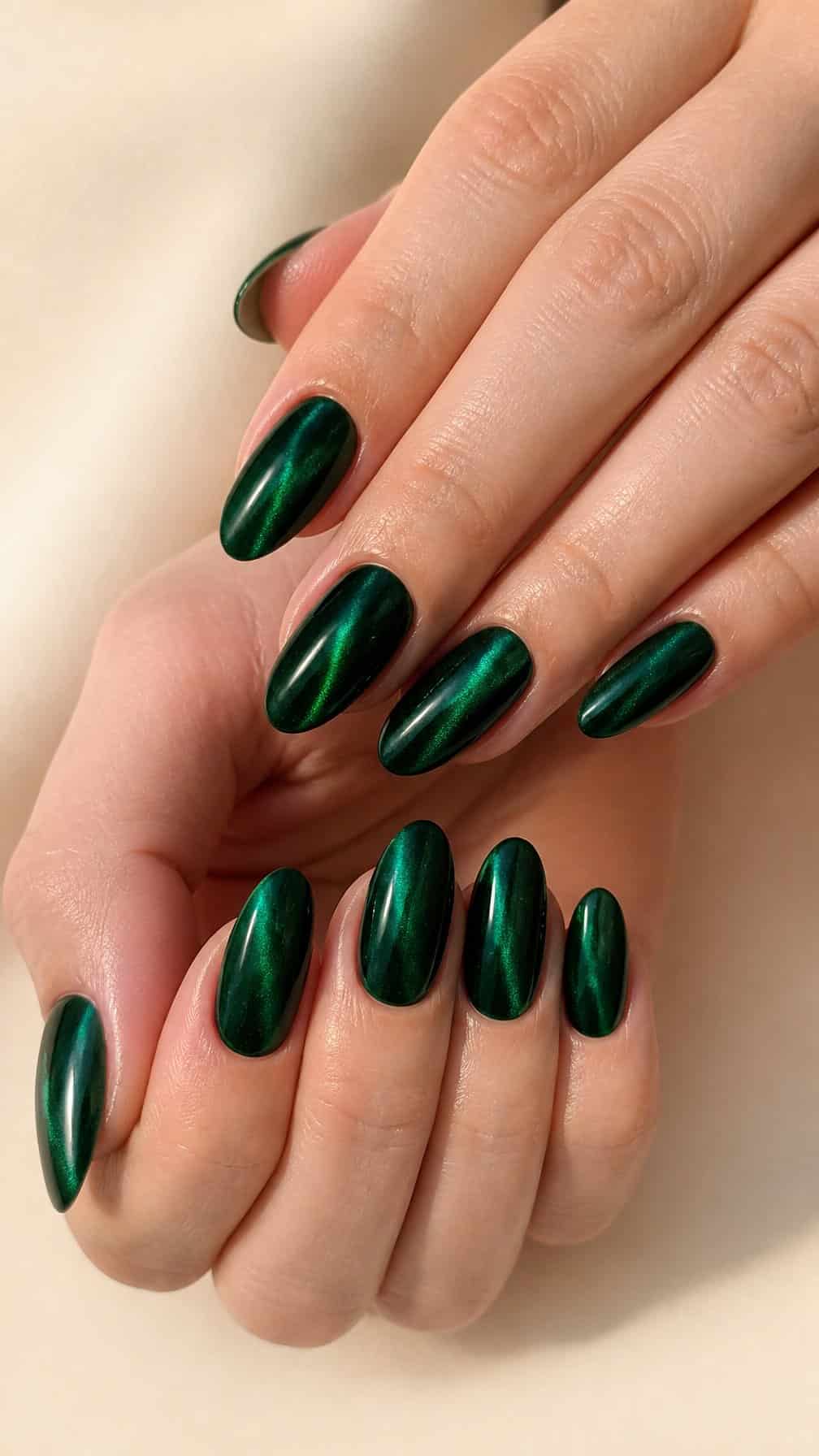 A close-up of hands with long almond-shaped emerald green cat-eye manicure.