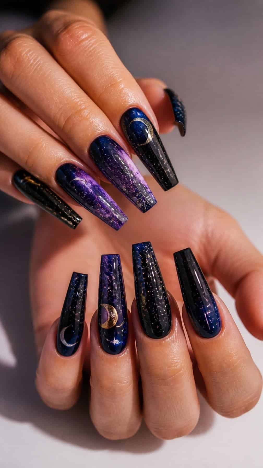 A close-up of hands showing long coffin-shaped nails decorated with stars, constellations, and crescent moons.