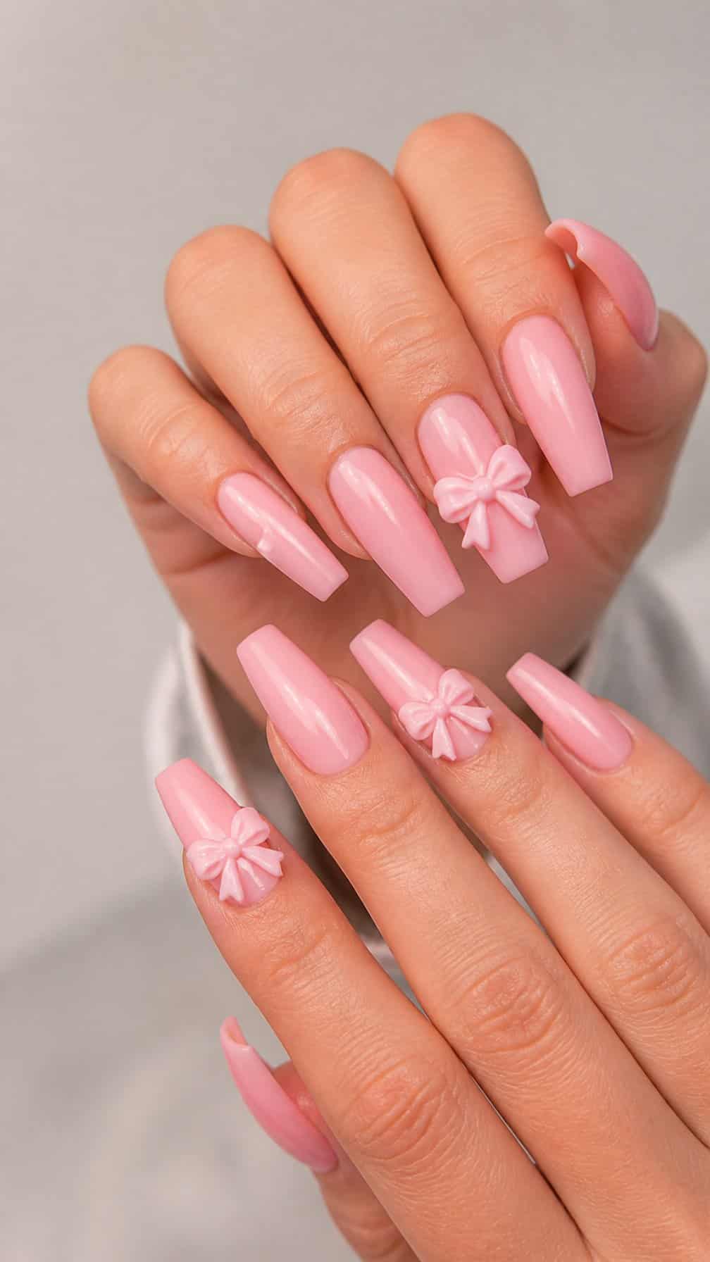 A close-up of long glossy pink nails decorated with raised three-dimensional bows.